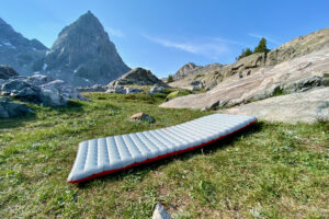 the nemo tensor all-season sleeping pad inflated for display on an alpine meadow with a rocky mountain backdrop on a sunny day