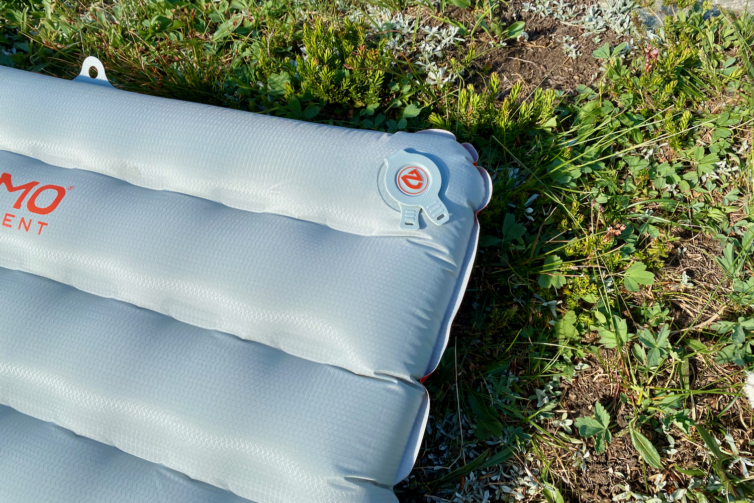 a close-up the corner of the nemo tensor all-season sleeping pad on a green meadow showing the square quilt like baffles for supportive sleep and a valve for inflating and deflating