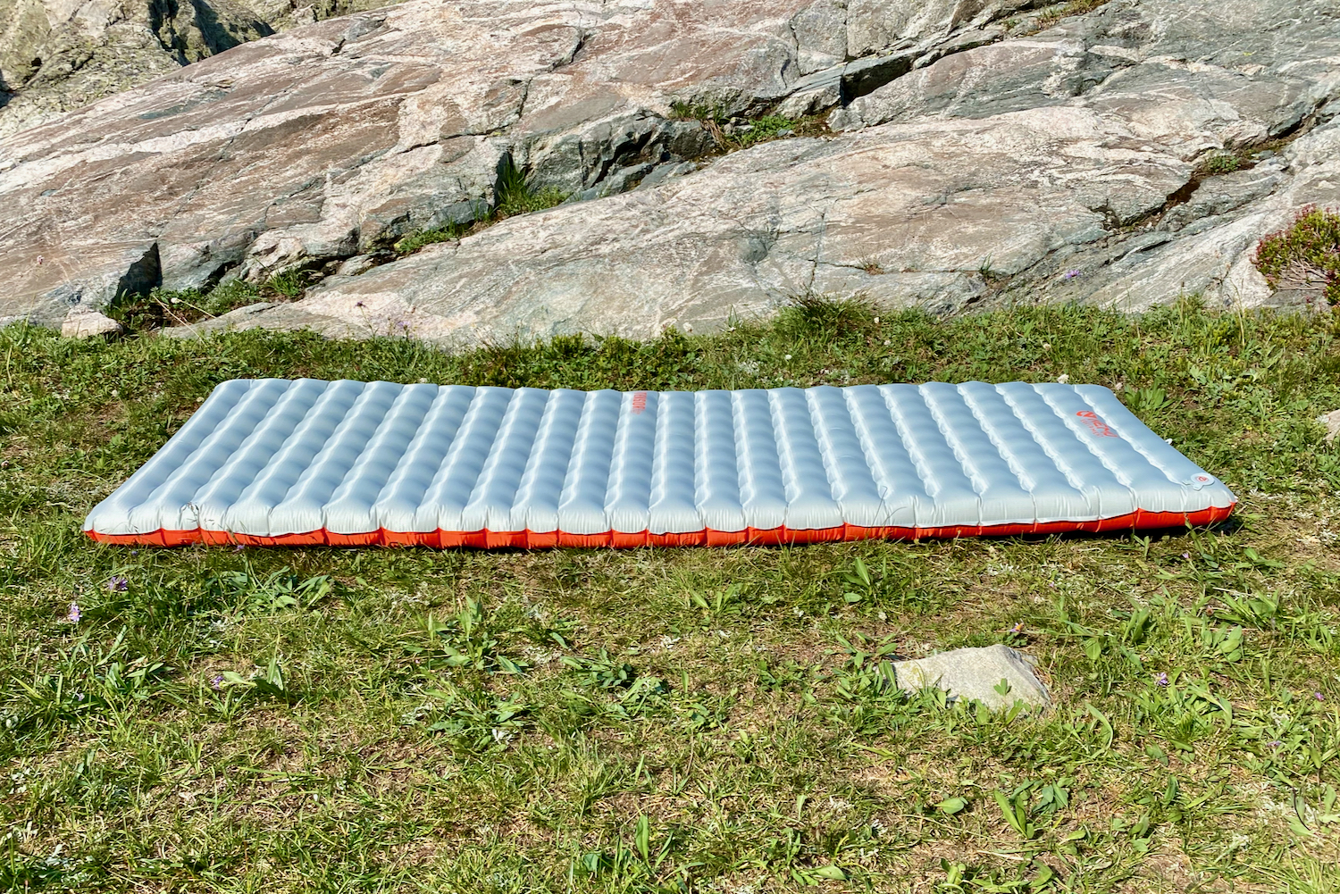 a side view of the two types of fabrics seamed together to make the nemo tensor all-season sleeping pad. the pad is laid atop green alpine grasses with rocky slabs behind