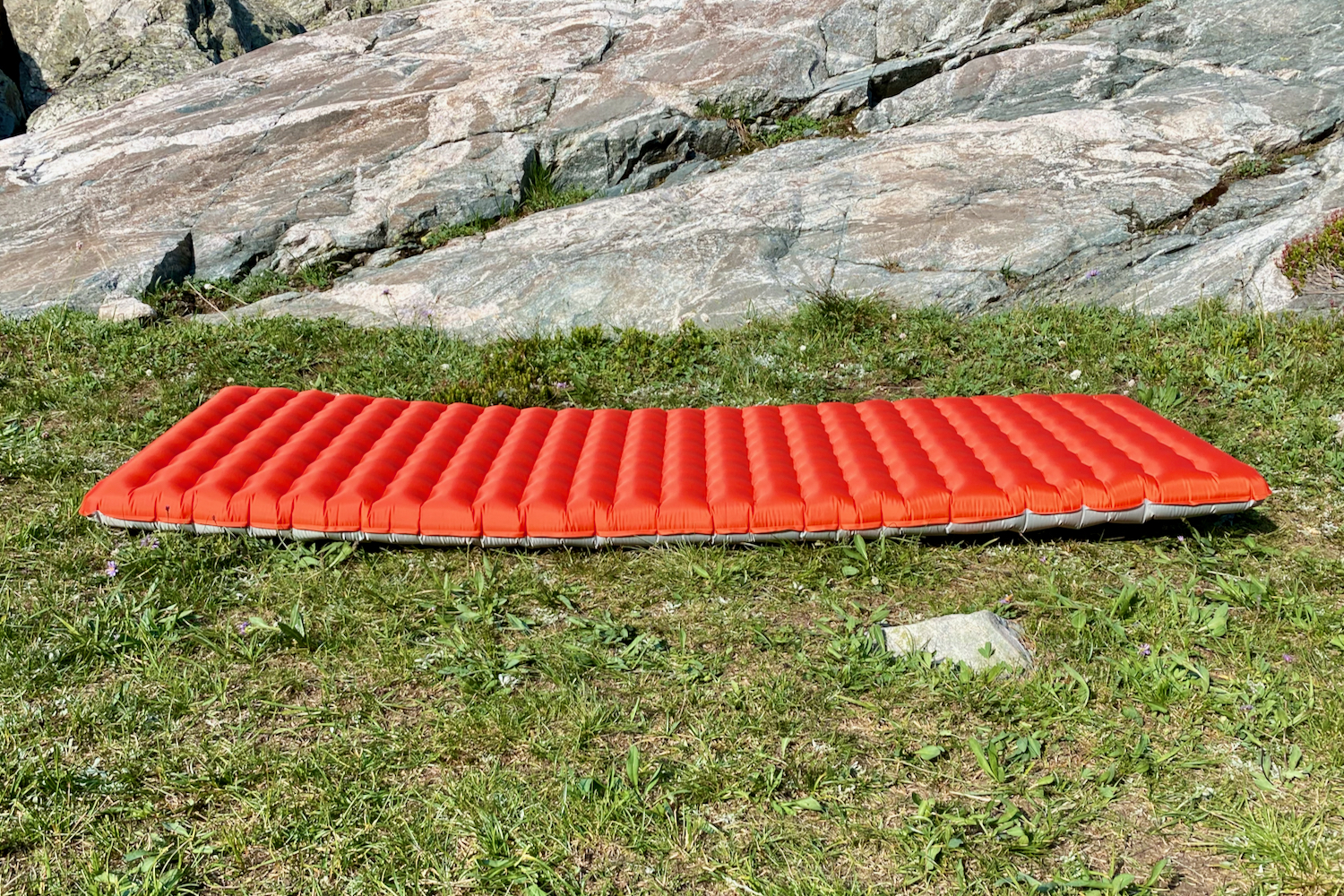 a NEMO tensor all-season sleeping pad on some alpine grass with a slabby rock behind resting upside down to show the red bottom fabric