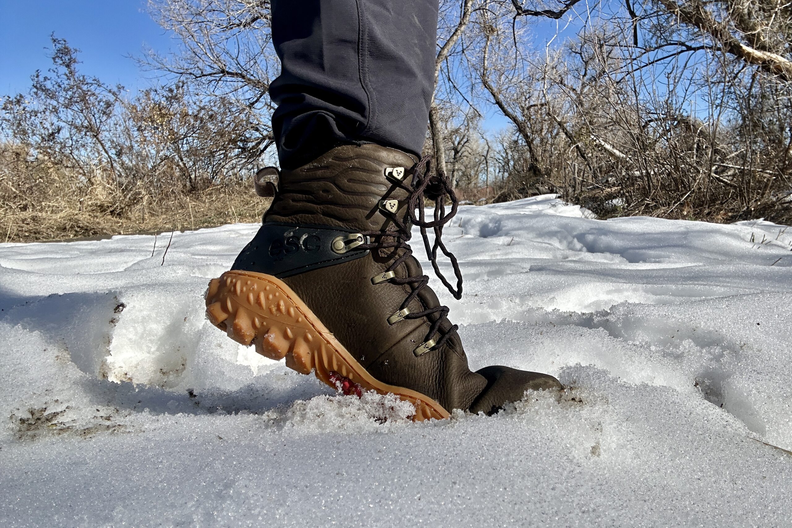 Close up image from knees down of a boot in the snow.