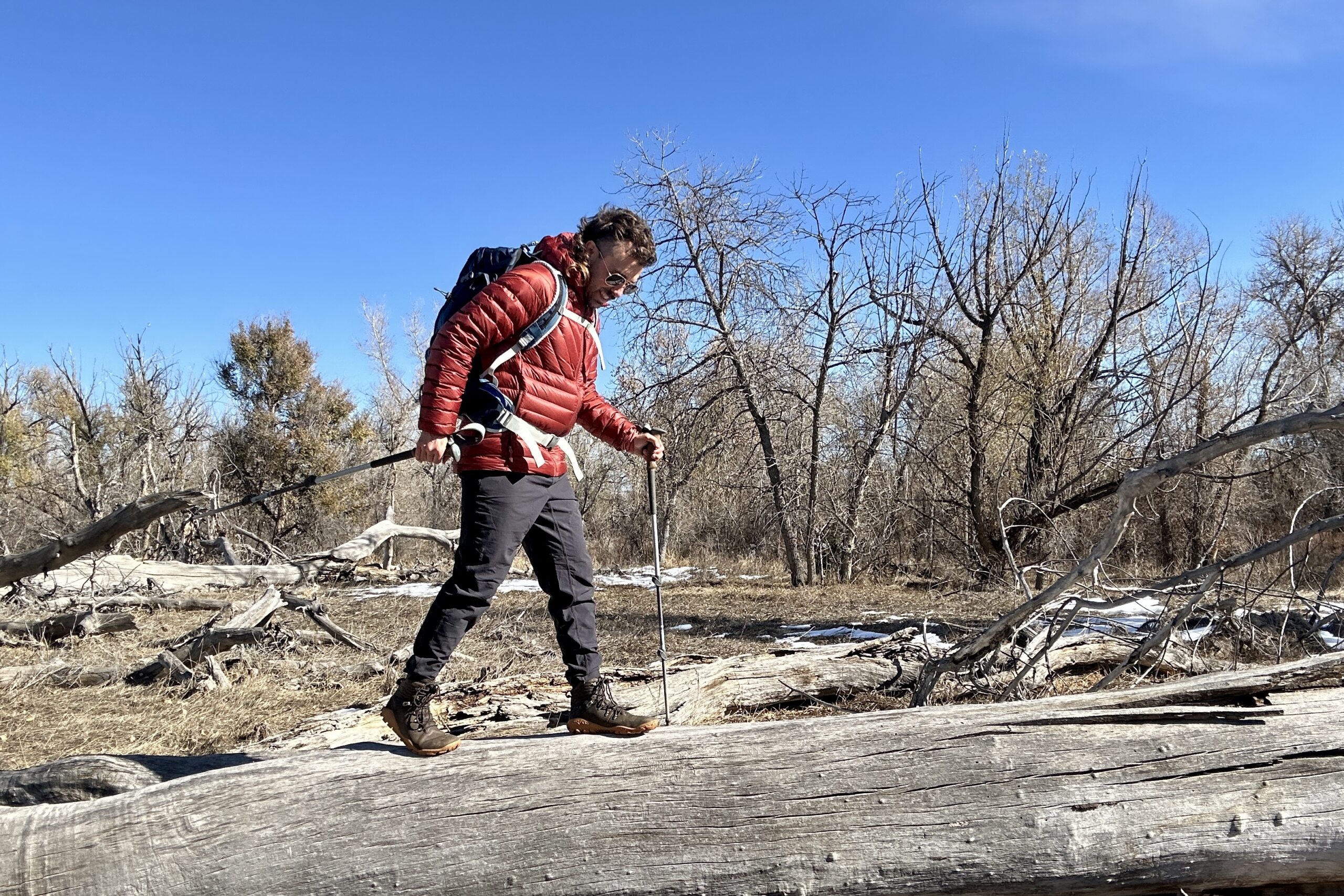 A hiker walks on a log in a wilderness area on a bluebird day.