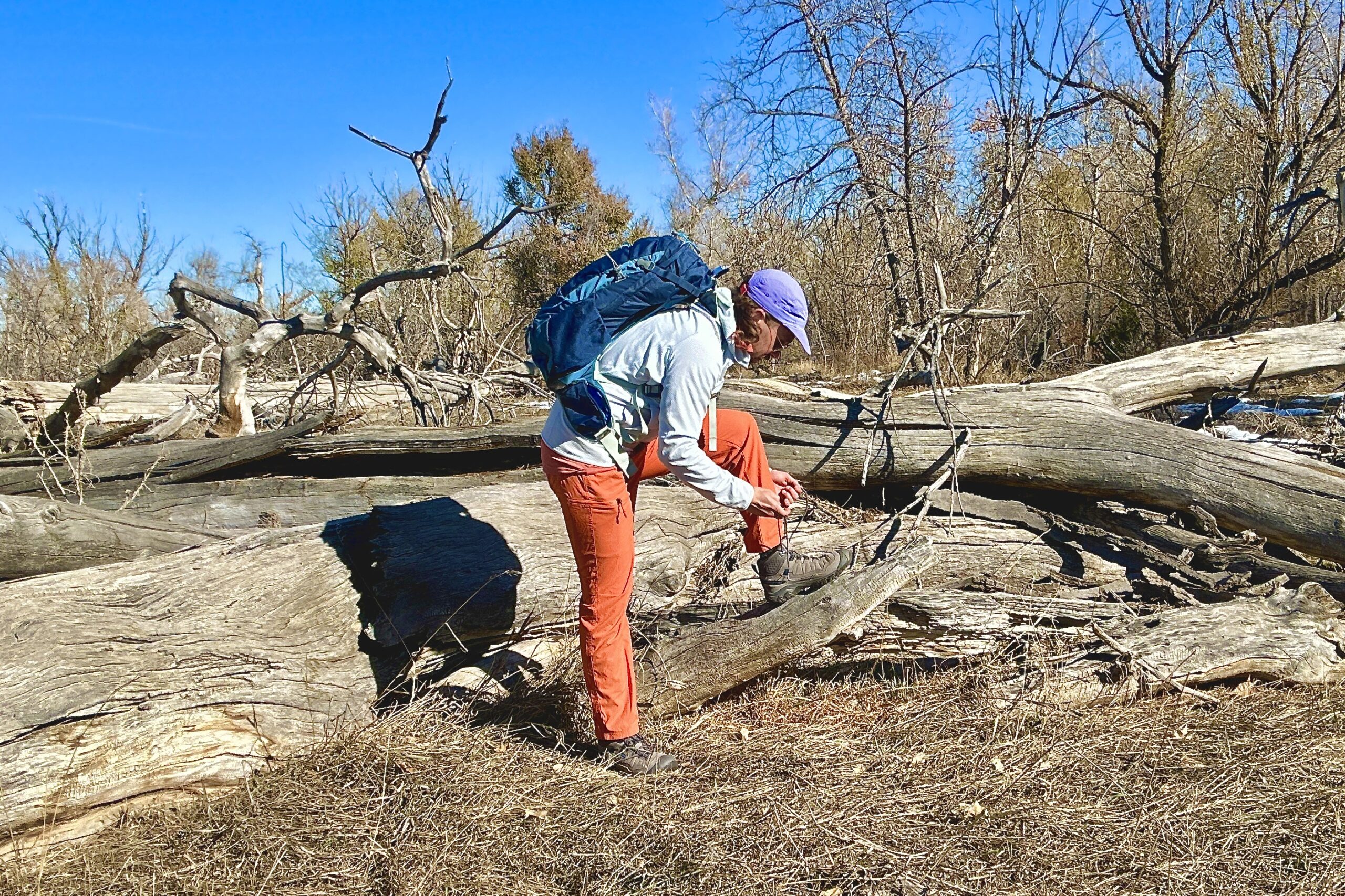 A man ties his shoes while propping his foot up on a log in a wilderness area.