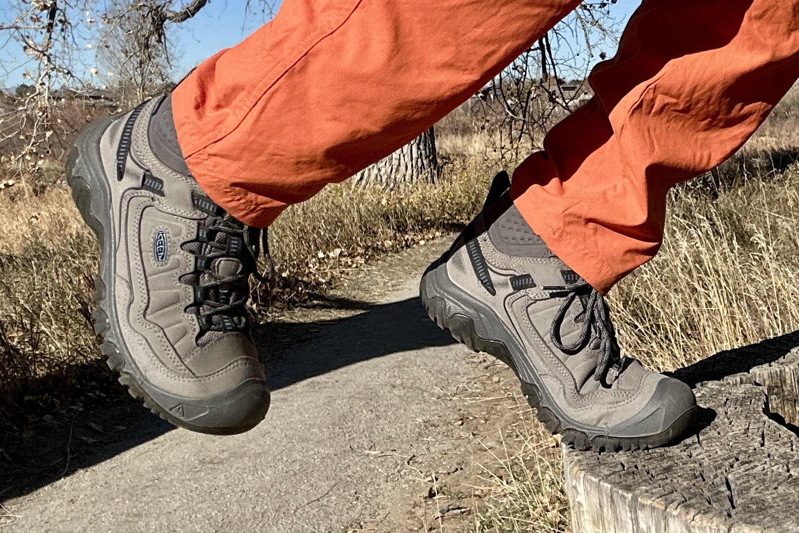 Close up image from knees down of a person stepping up onto a log with the focus on their hiking boots.