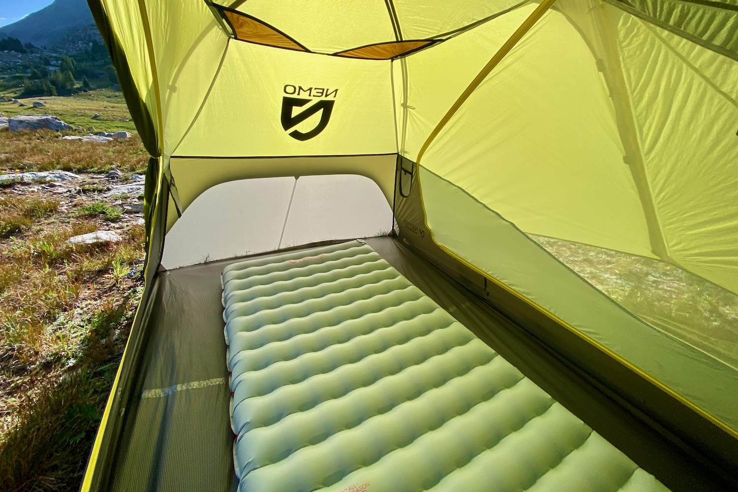 a green tent casts its glow on a silver sleeping pad with the door of the tent open on a sunny day.