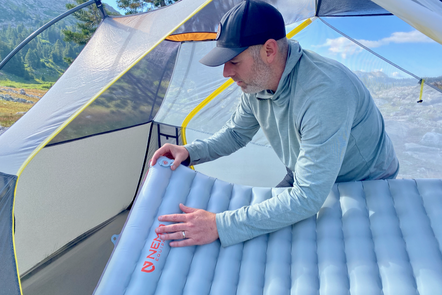 a backpacker touching the valve of their inflated sleeping pad while inside their tent