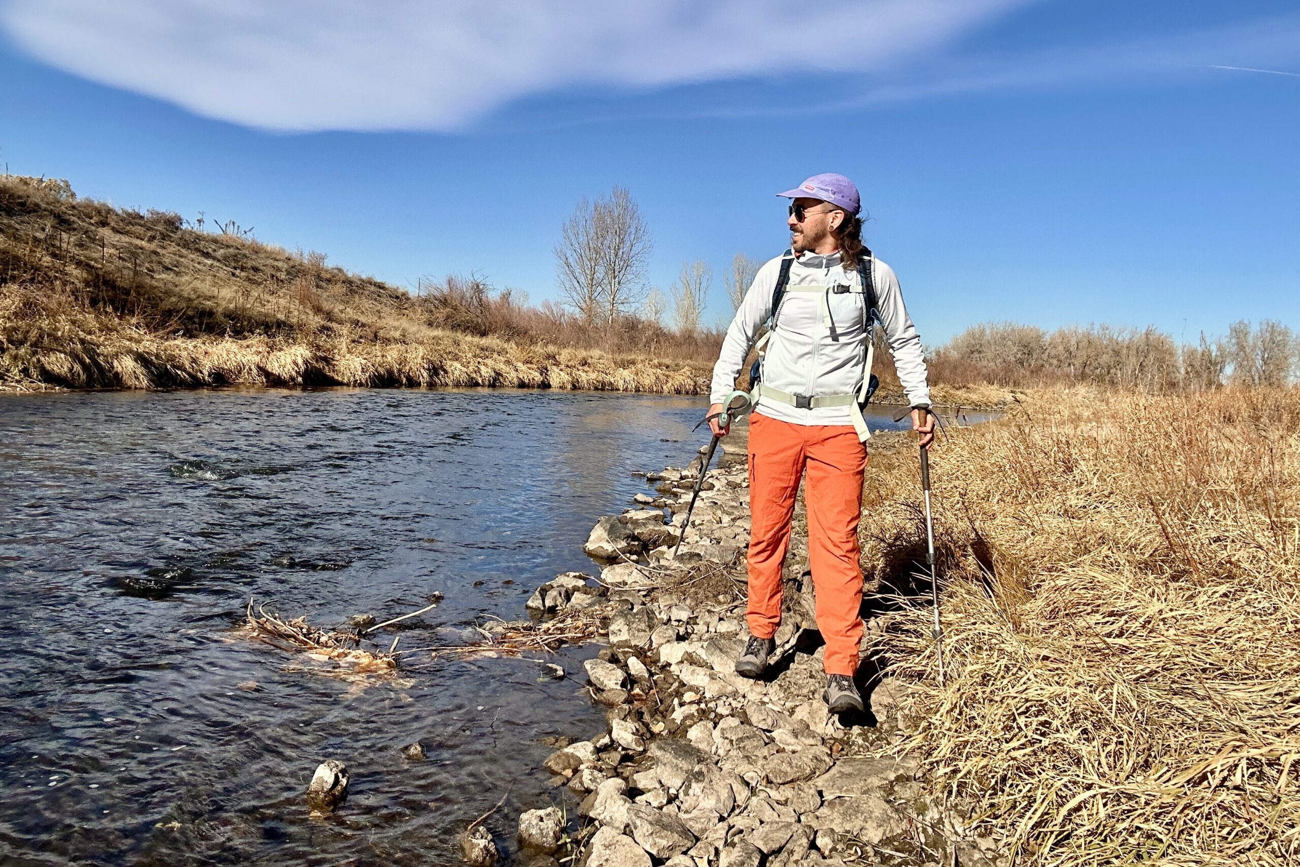 A hiker walks along a river looking off in the distance.