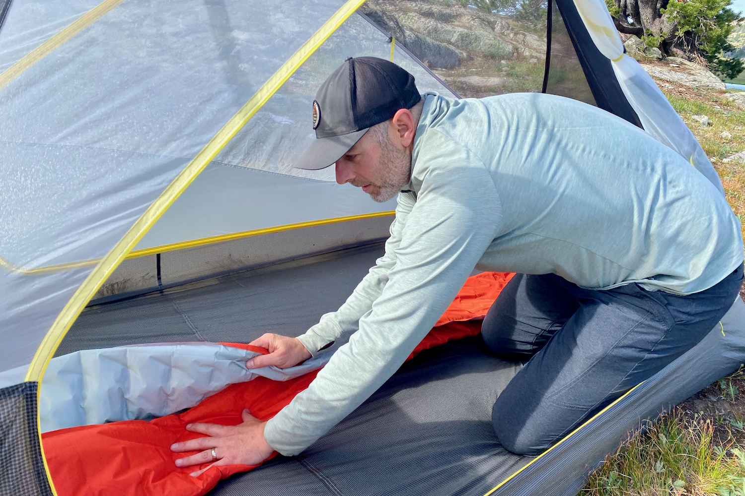 a backpacker inside their tent folding their sleeping pad to pack it up.