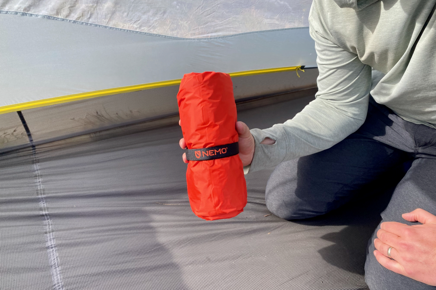 a backpacker holds up their packed sleeping pad while inside their tent to show how small it is