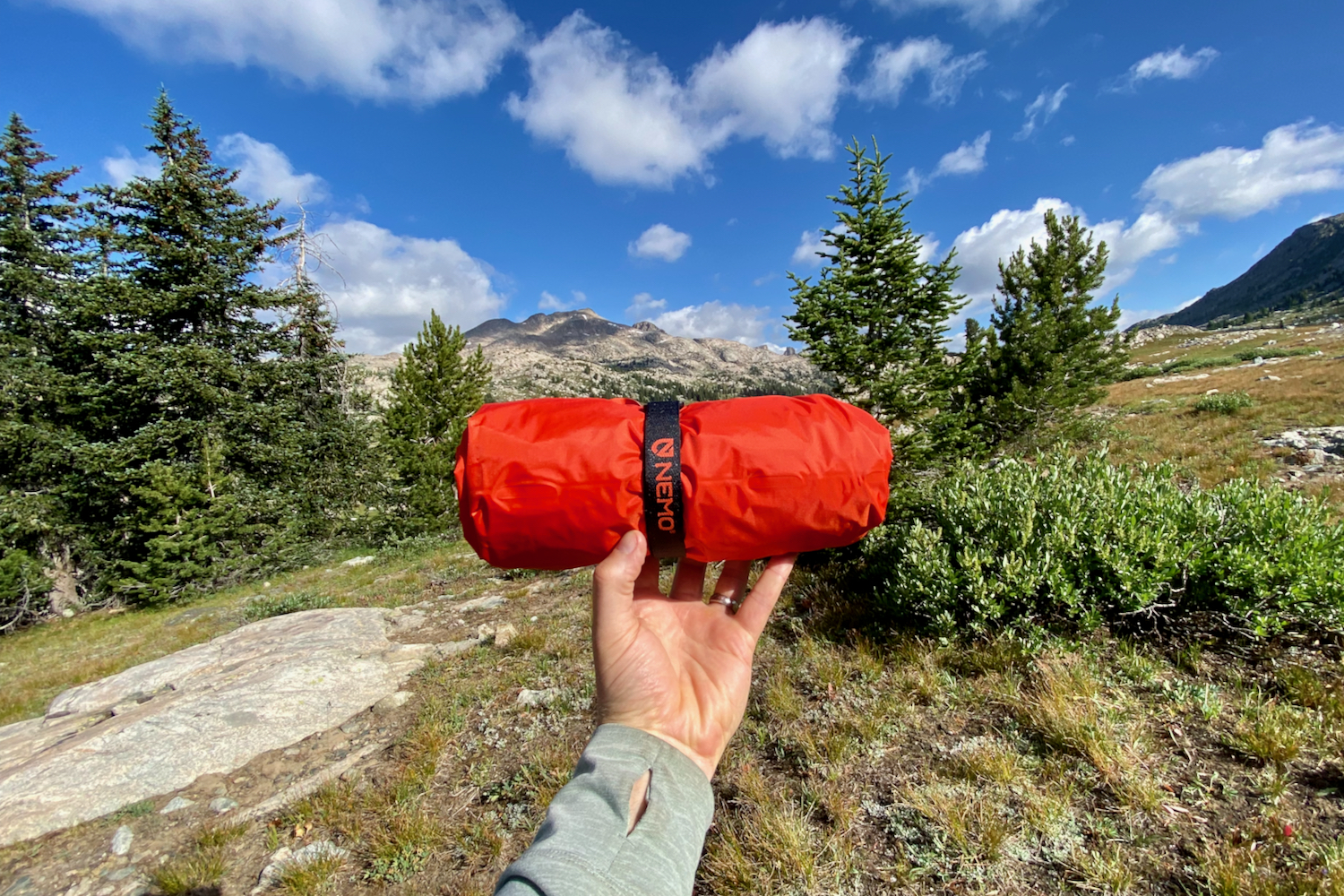 a backpacker's arm and hand holding the packed nemo tensor all-season sleeping pad in its red stuff sack