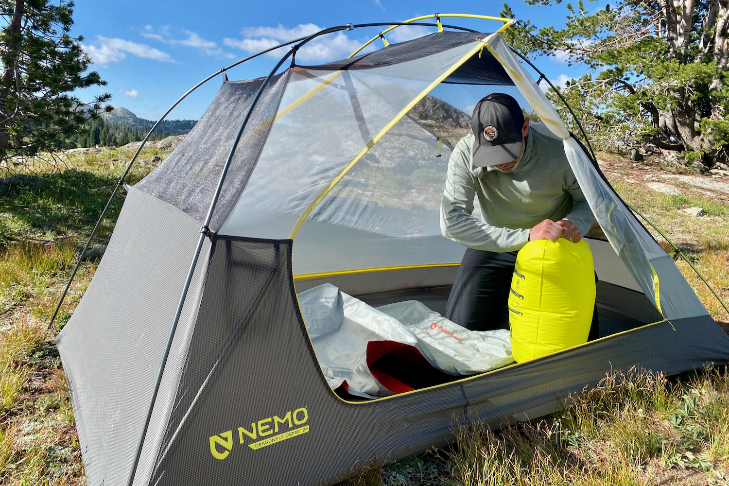 a backpacker inflates their nemo tensor all-season with a neon green pump sack while inside their tent.