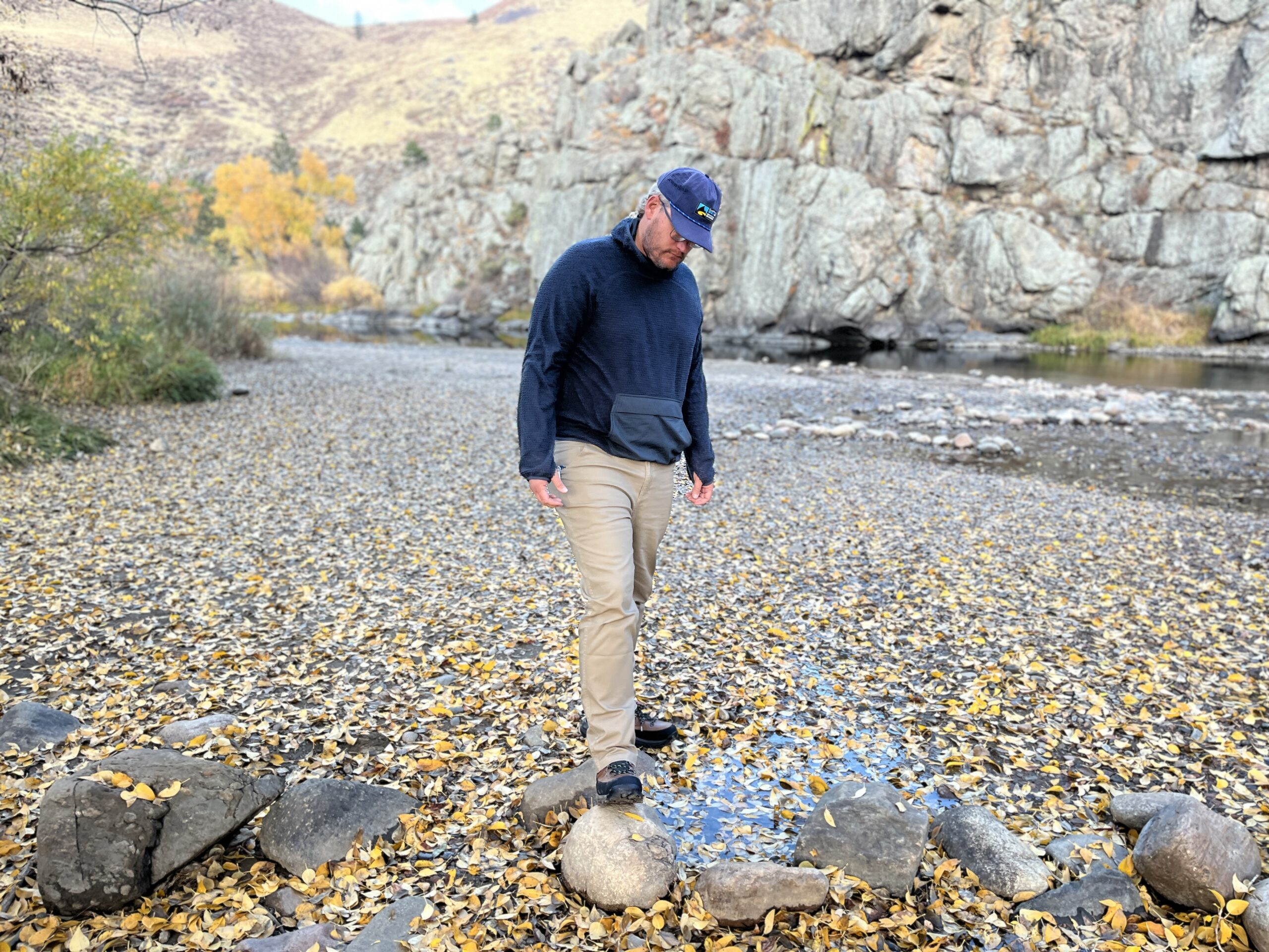 a man walks on some rocks covered in yellow aspen leaves next to a river