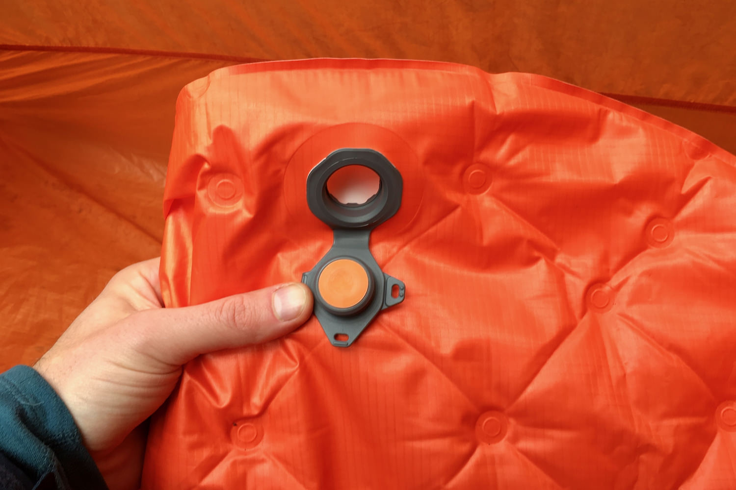 a hand holding open the dump valve on the sea to summit ultralight insulated sleeping pad to show how to quickly deflate the pad when packing up