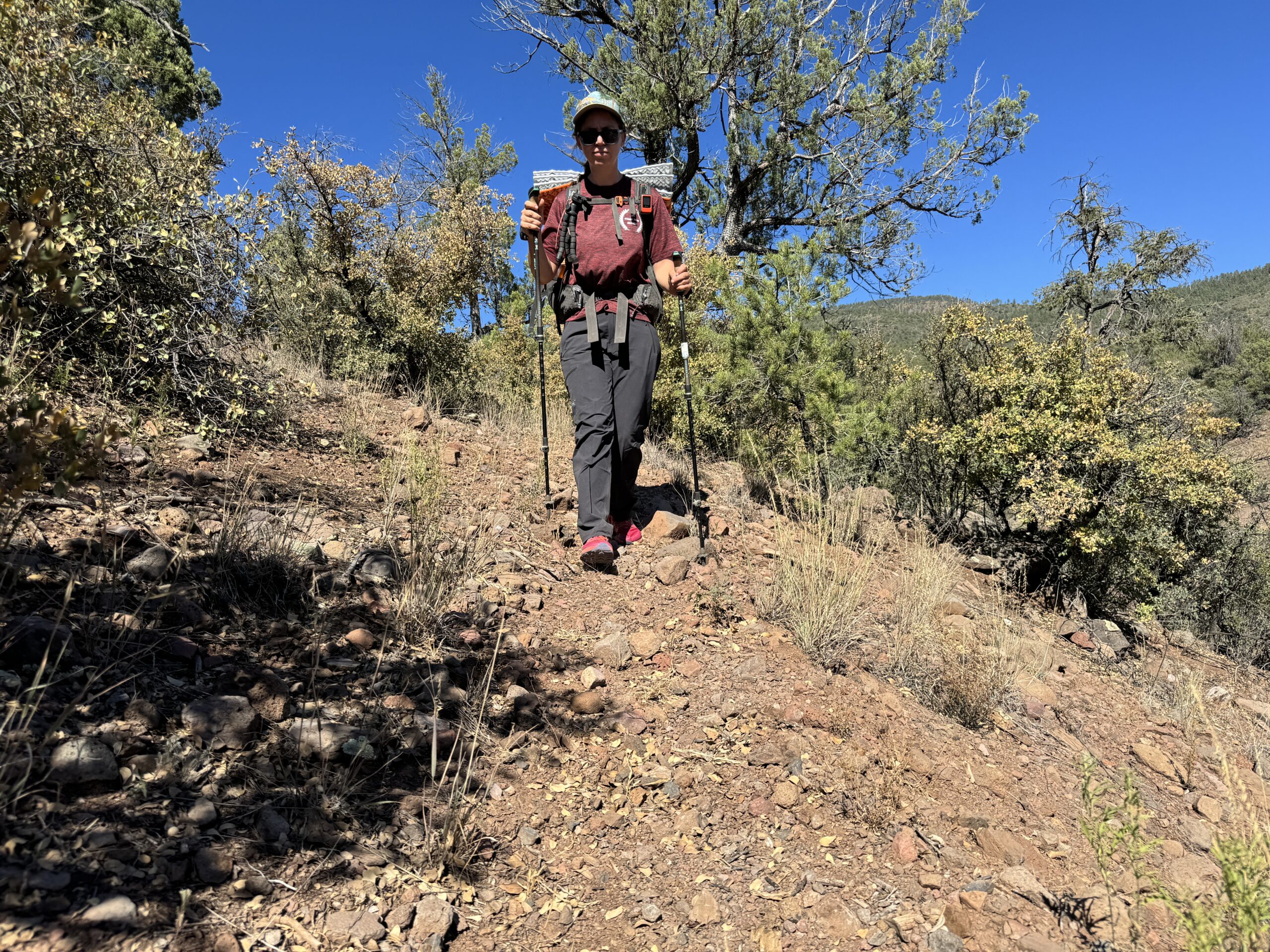 A person wearing the Gamma pants and a backpack is walking down a trail in the woods.