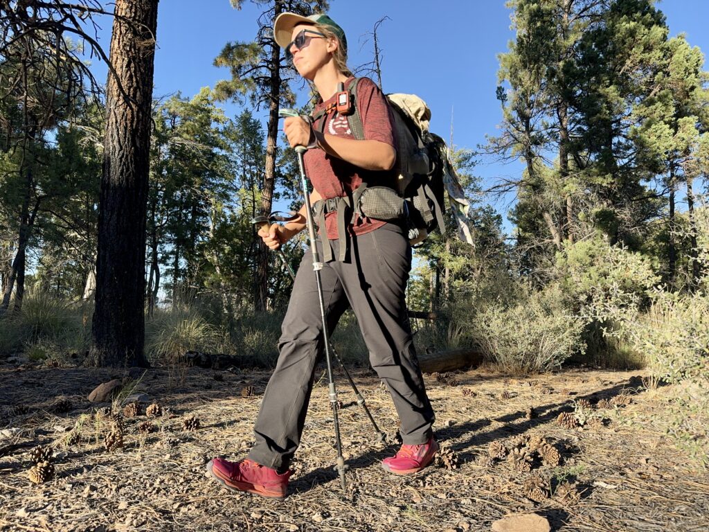 A person wearing the Gamma pants and a backpack is walking down a trail in the woods.