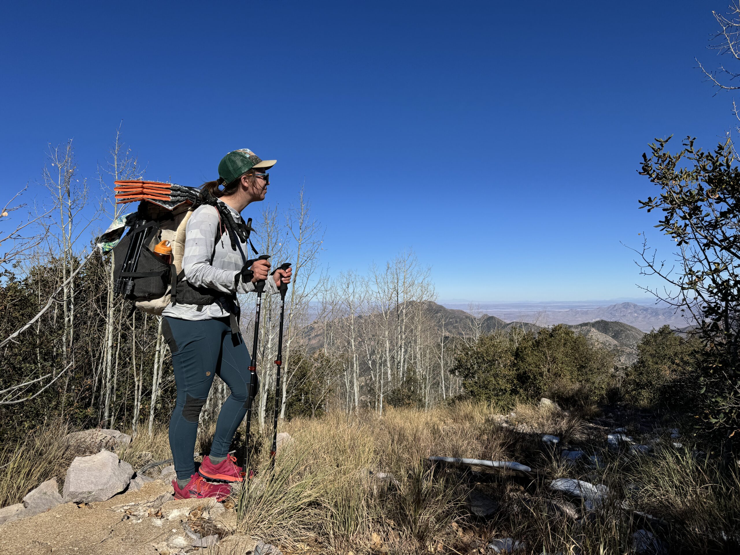 A person wearing the Abisko leggings and a backpack is admiring a view from the top of a mountain.