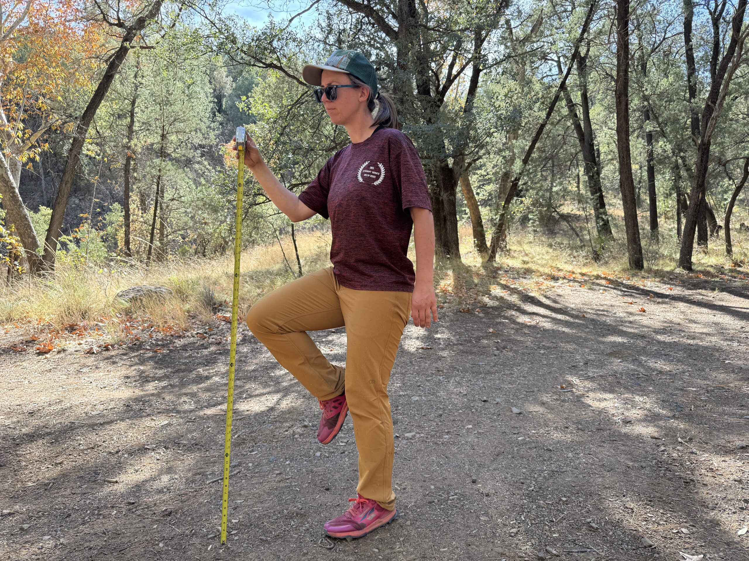 A person stands on one foot while holding the other knee up. A measuring tape is extended next to the raised knee to test for mobility of the Ferrosi Pants.