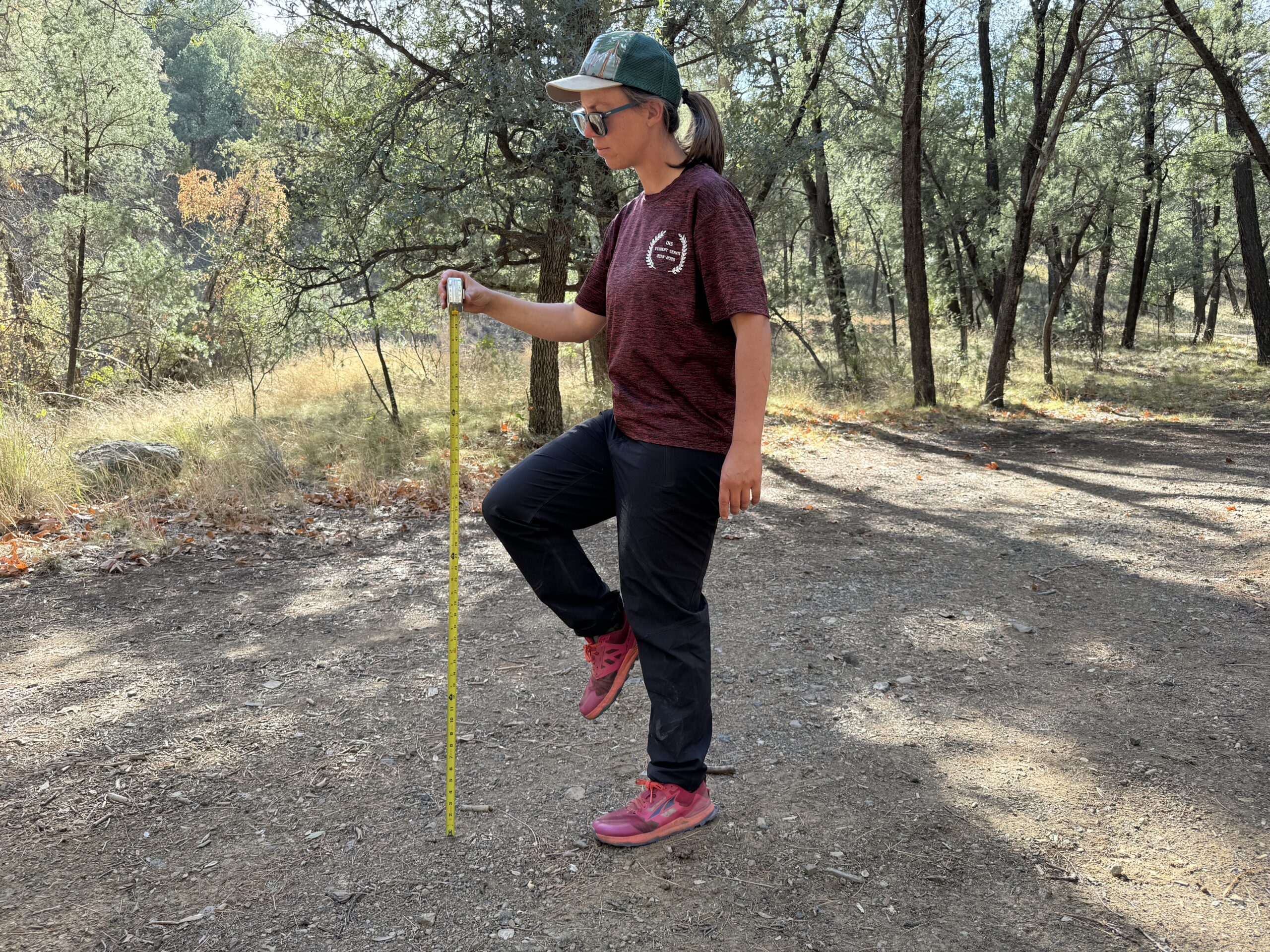 A person stands on one foot while holding the other knee up. A measuring tape is extended next to the raised knee to test for mobility of the Arc'teryx Gamma Pants.