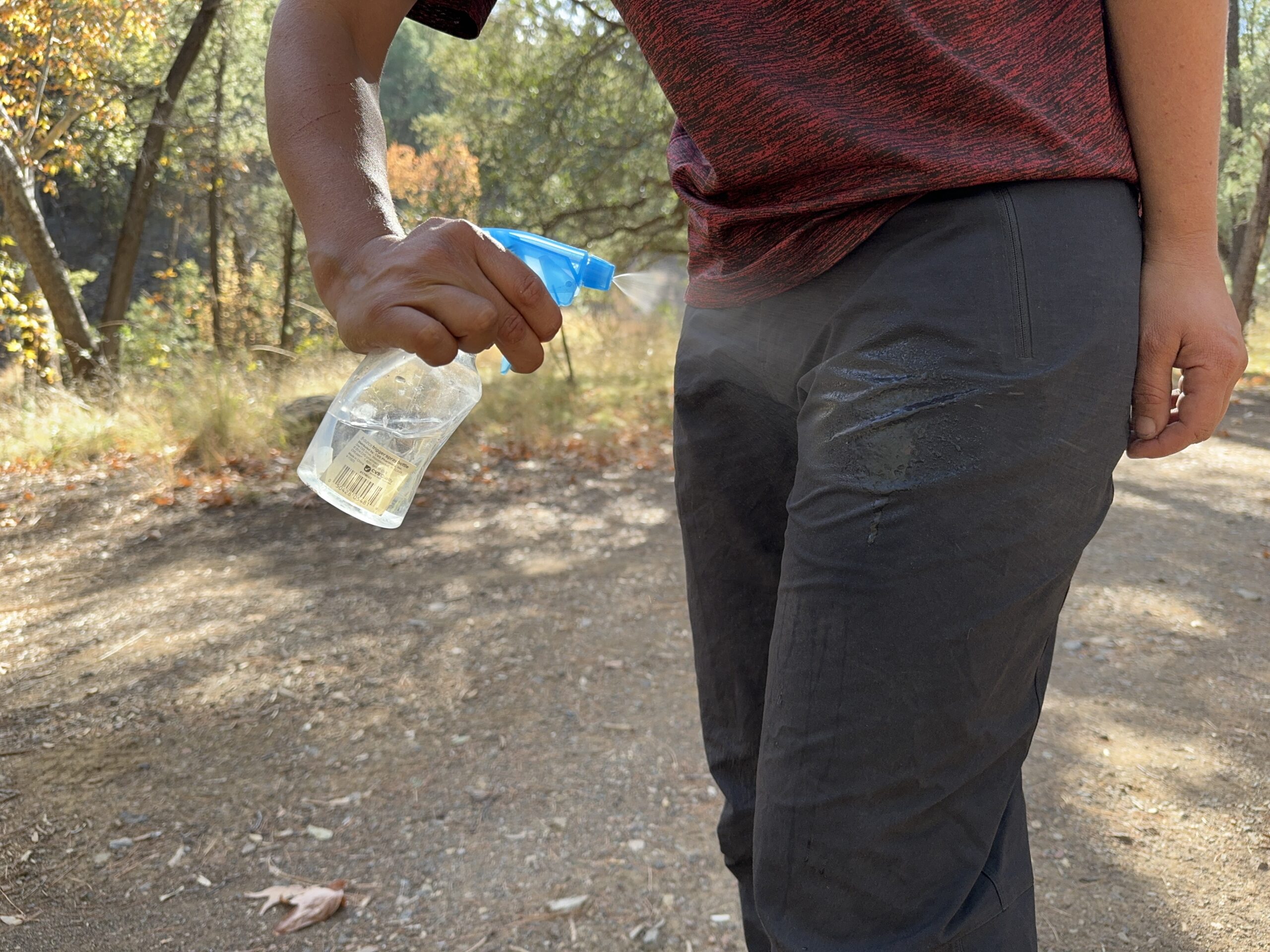 A hand is spraying the Arc'teryx Gamma pants with water from a squirt bottle.