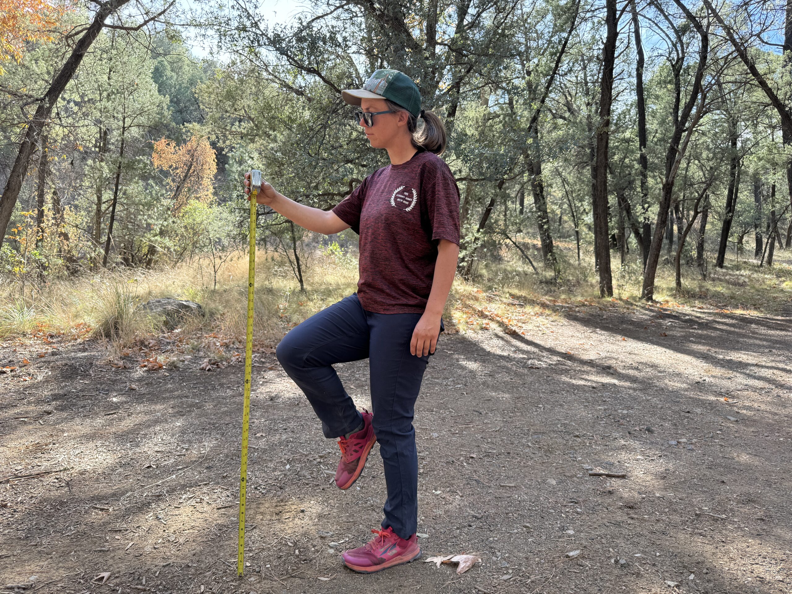 A person stands on one foot while holding the other knee up. A measuring tape is extended next to the raised knee to test for mobility of the Halle pants.