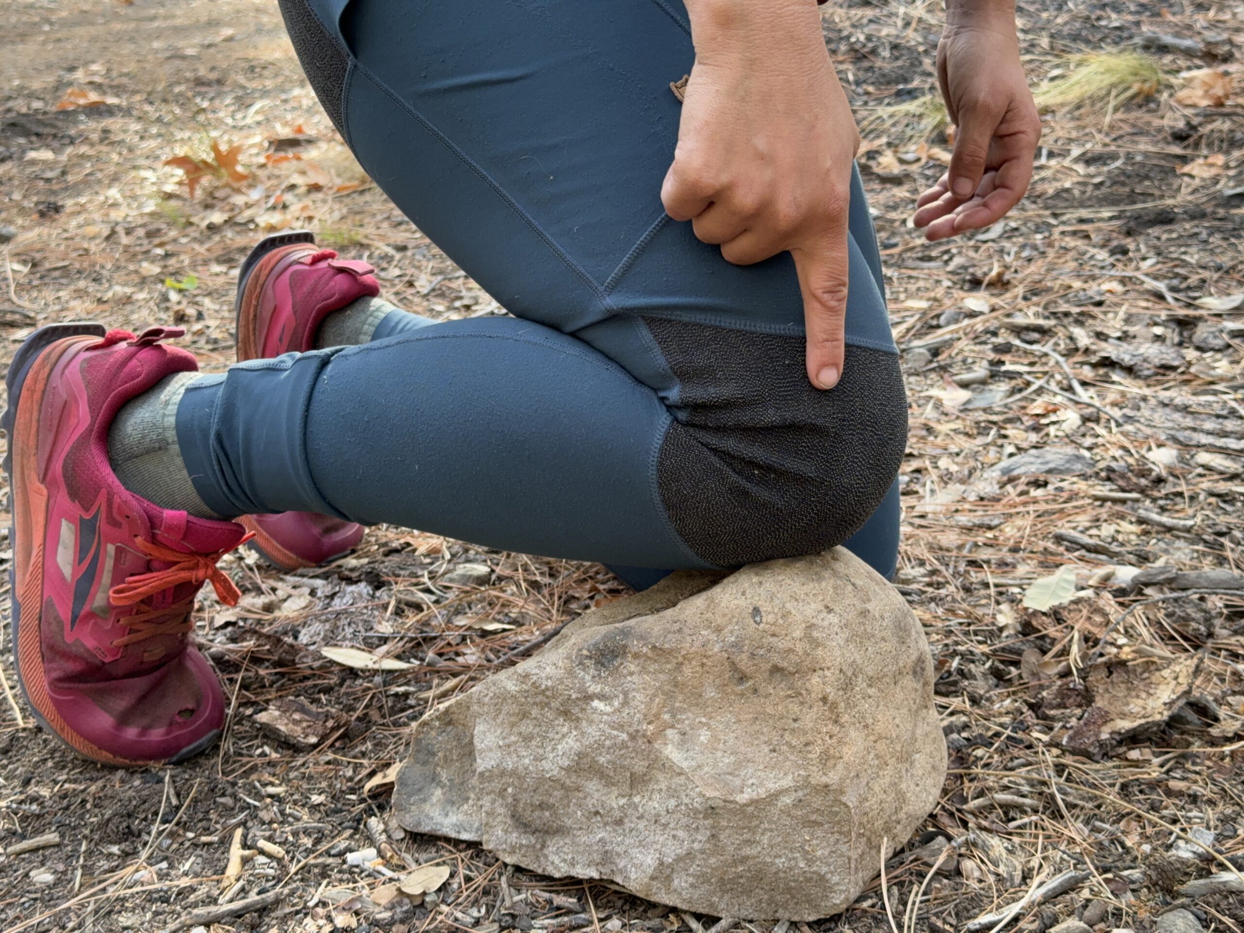 The reinforced knee of the Abisko leggings are resting on a rock with a finger pointing out this feature.