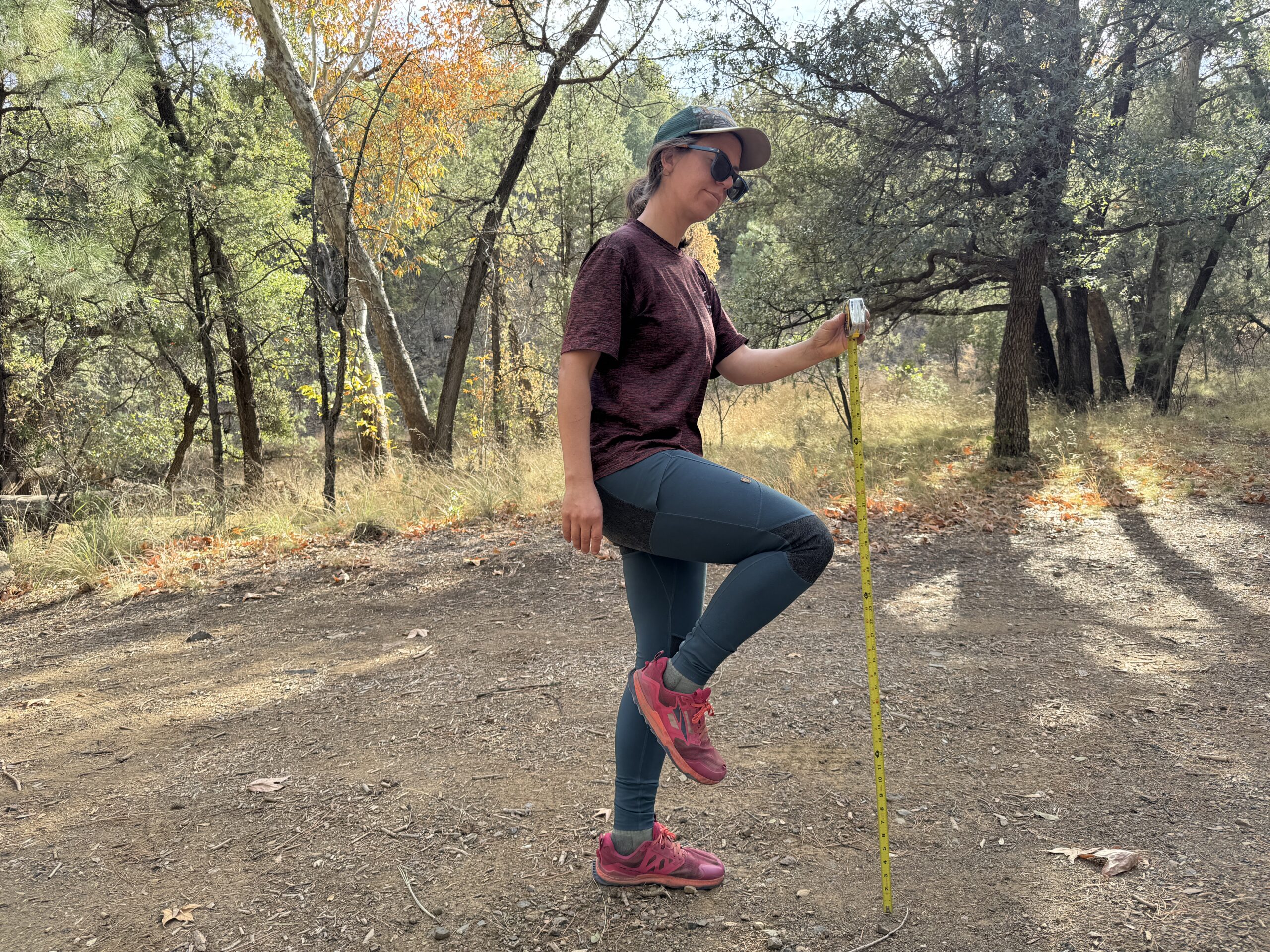 A person stands on one foot while holding the other knee up. A measuring tape is extended next to the raised knee to test for mobility of the Abisko Pants.