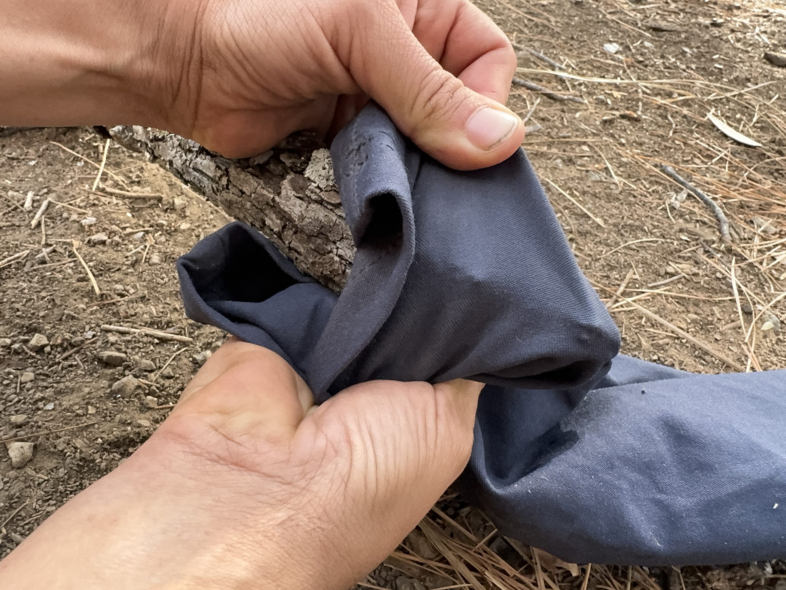 Close up of two hands stretching the fabric of the prAna Halle Straight pants over a sharp stick.