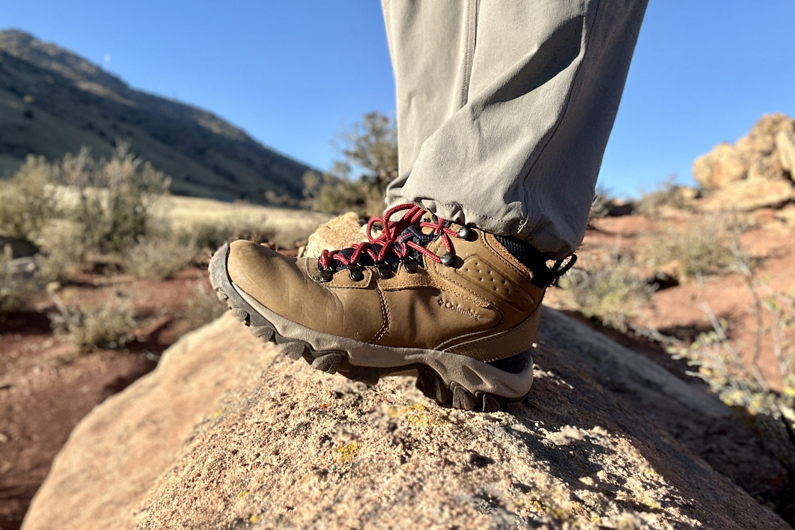 Close up from knees down of a person walking in hiking boots on a rock in the sun.