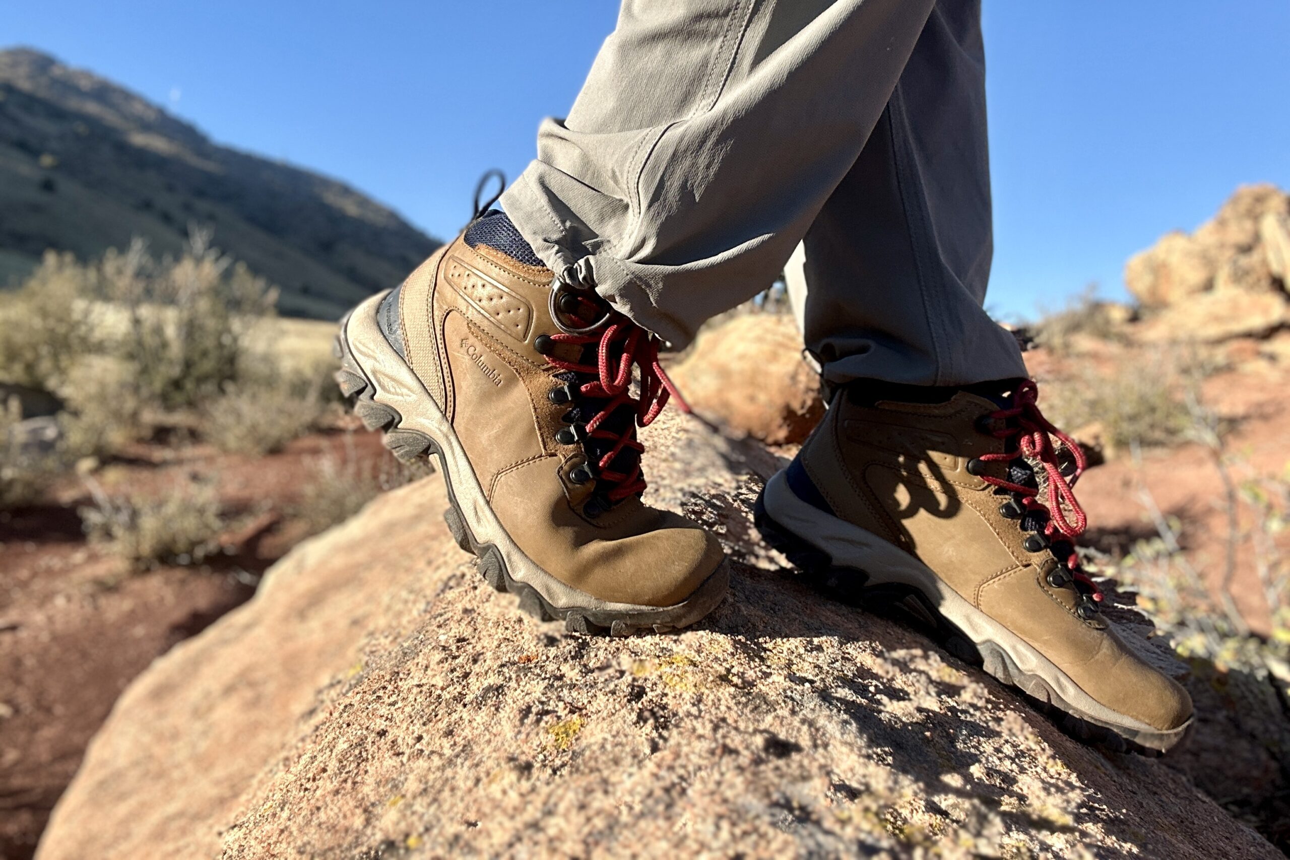 Close up from knees down of a person walking in hiking boots on a rock in the sun.