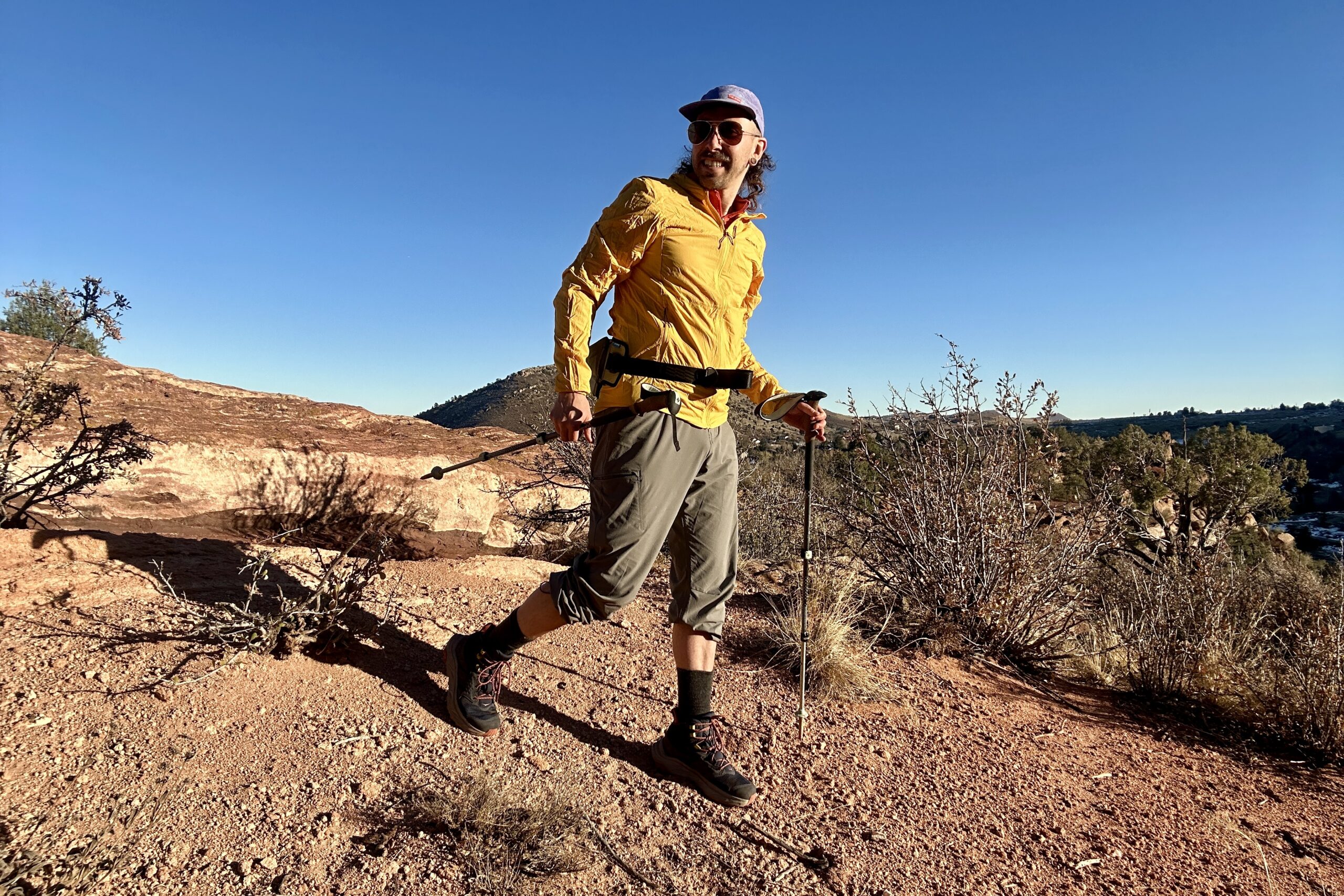 A man in a yellow jacket poses in a desert setting looking off-camera.