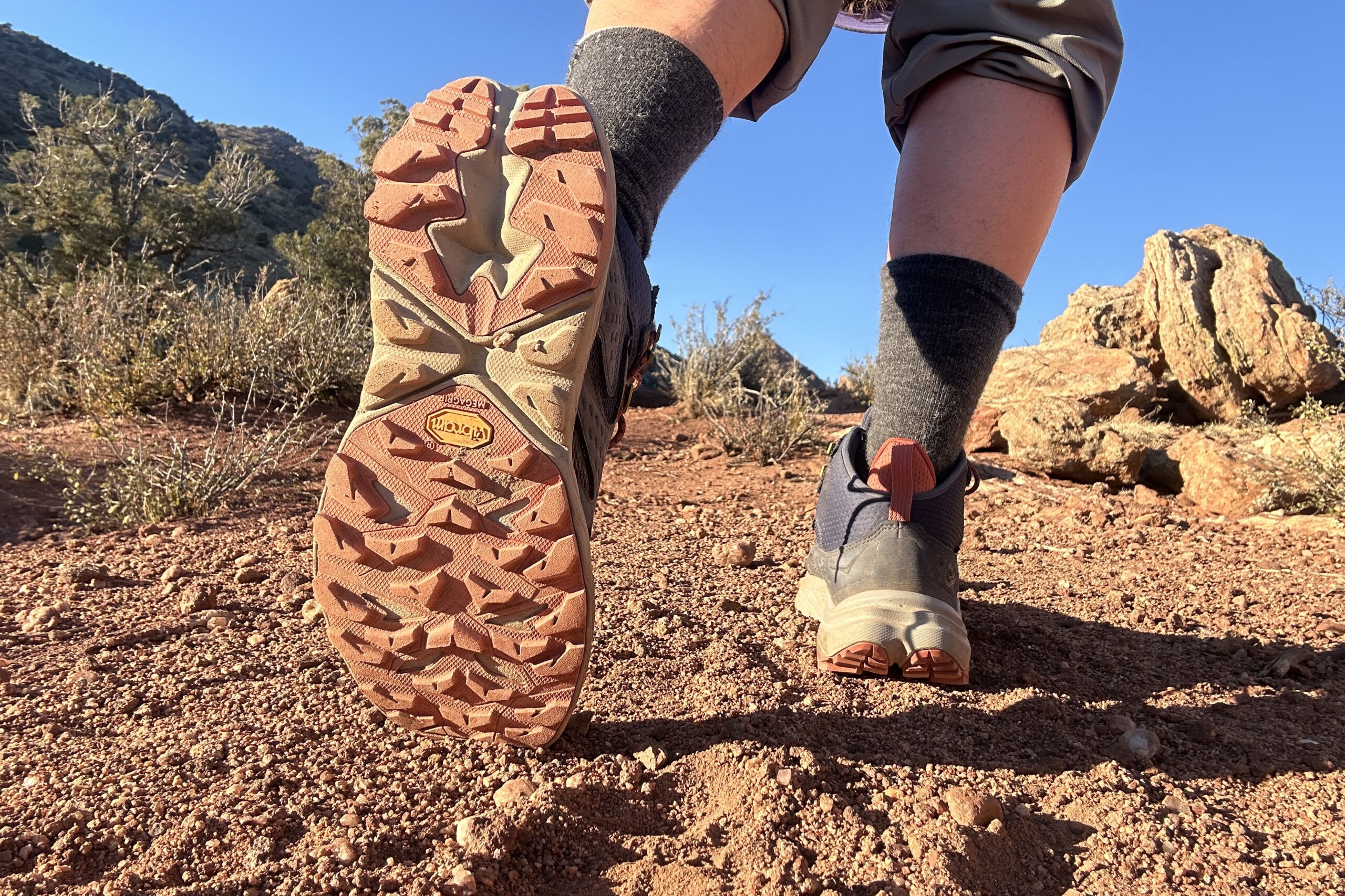 Close up from knees down of a person walking in hiking boots away from the camera. You can see the traction on one shoe.