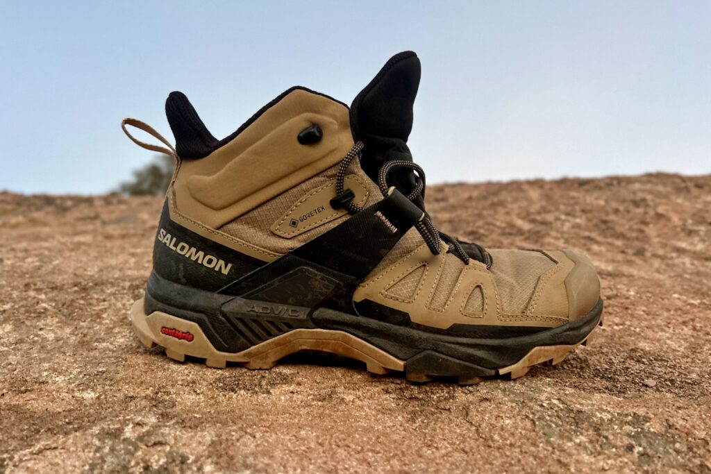 Close up of a single hiking boot posed on a rock facing right.