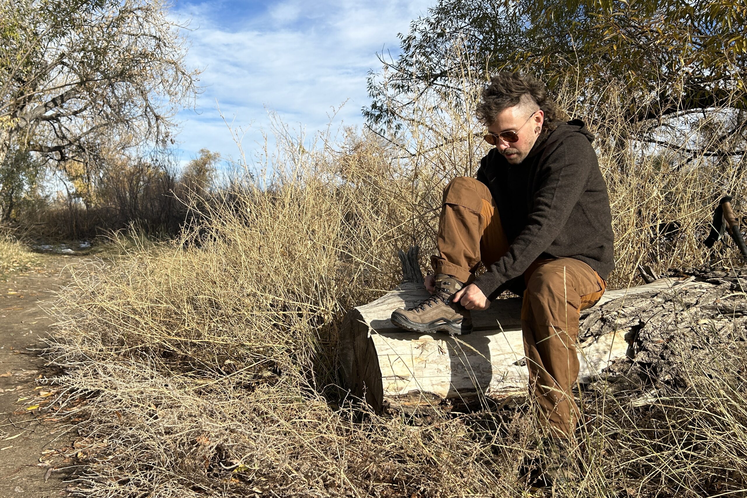 A man ties his boots while sitting on a log in a wilderness area.