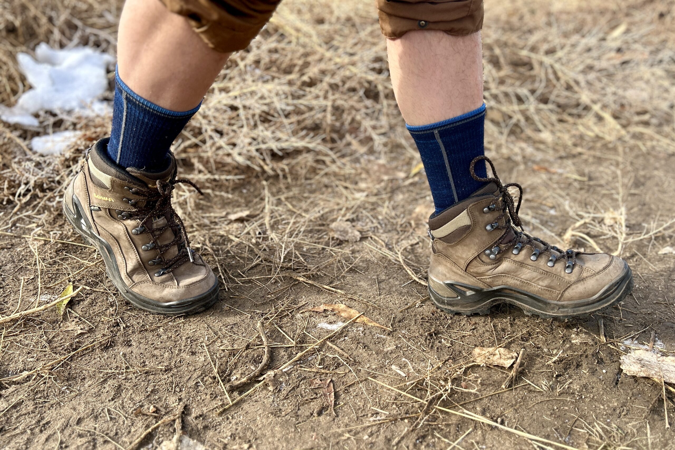 Close-up image from the knees down of a person walking in hiking boots in a wilderness area.