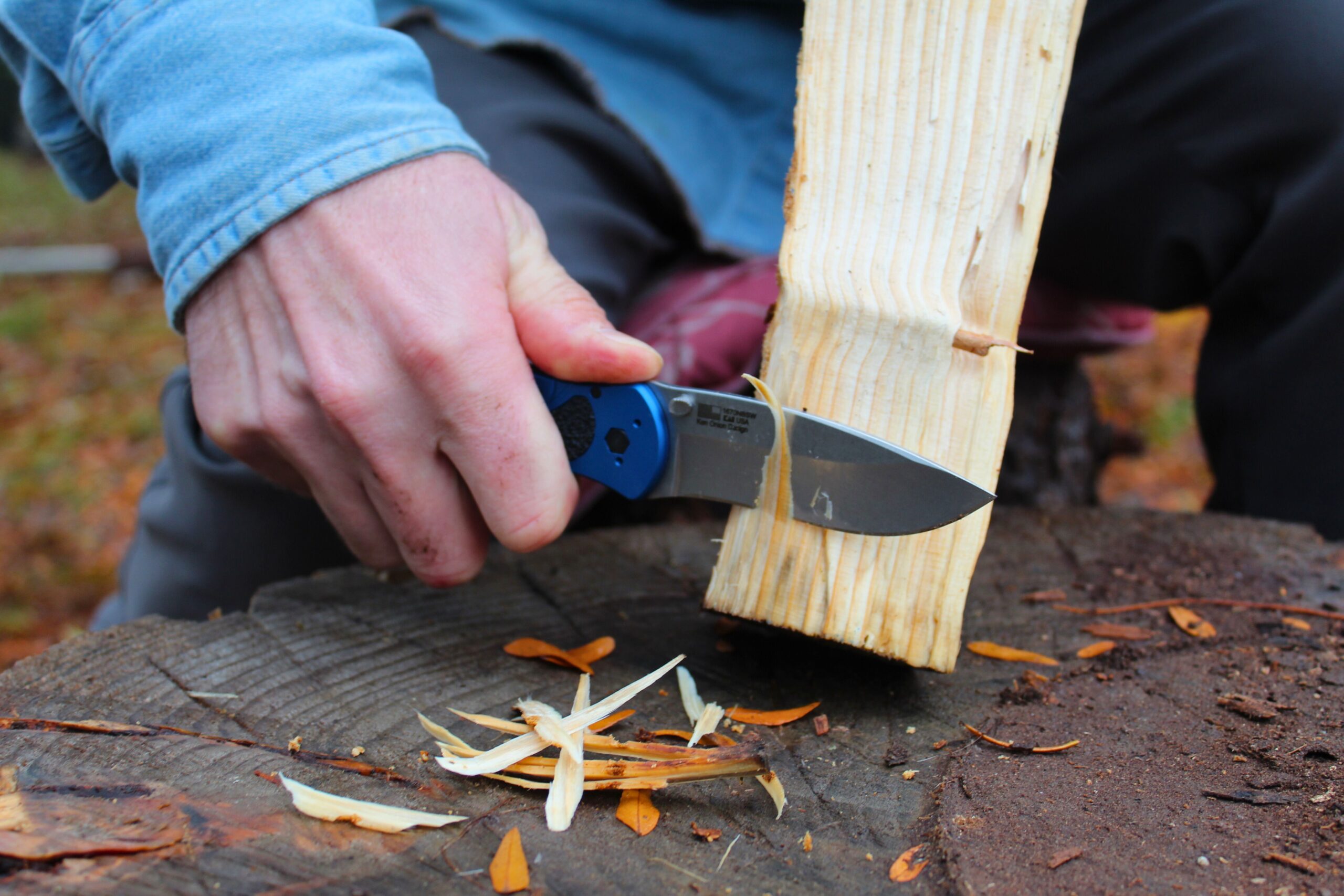 Using the Kershaw Blur pocket knife to cut shavings off a piece of fire wood