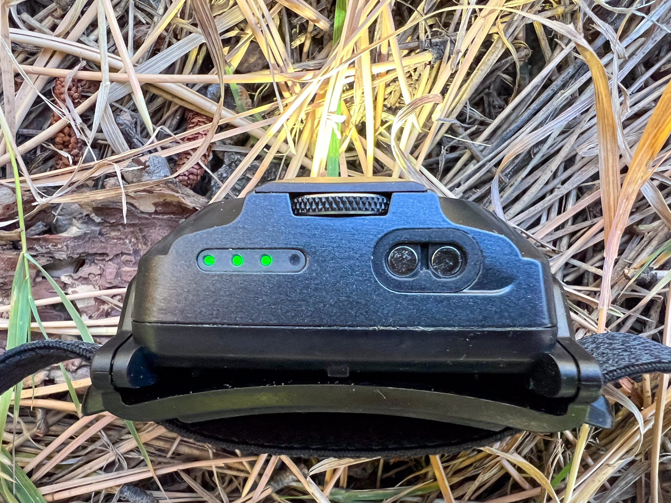 The image shows the Ledlenser HF6R Signature headlamp sitting in brown grass. The headlamp is on and the battery life indicator is illuminated indicating 75 percent battery life.