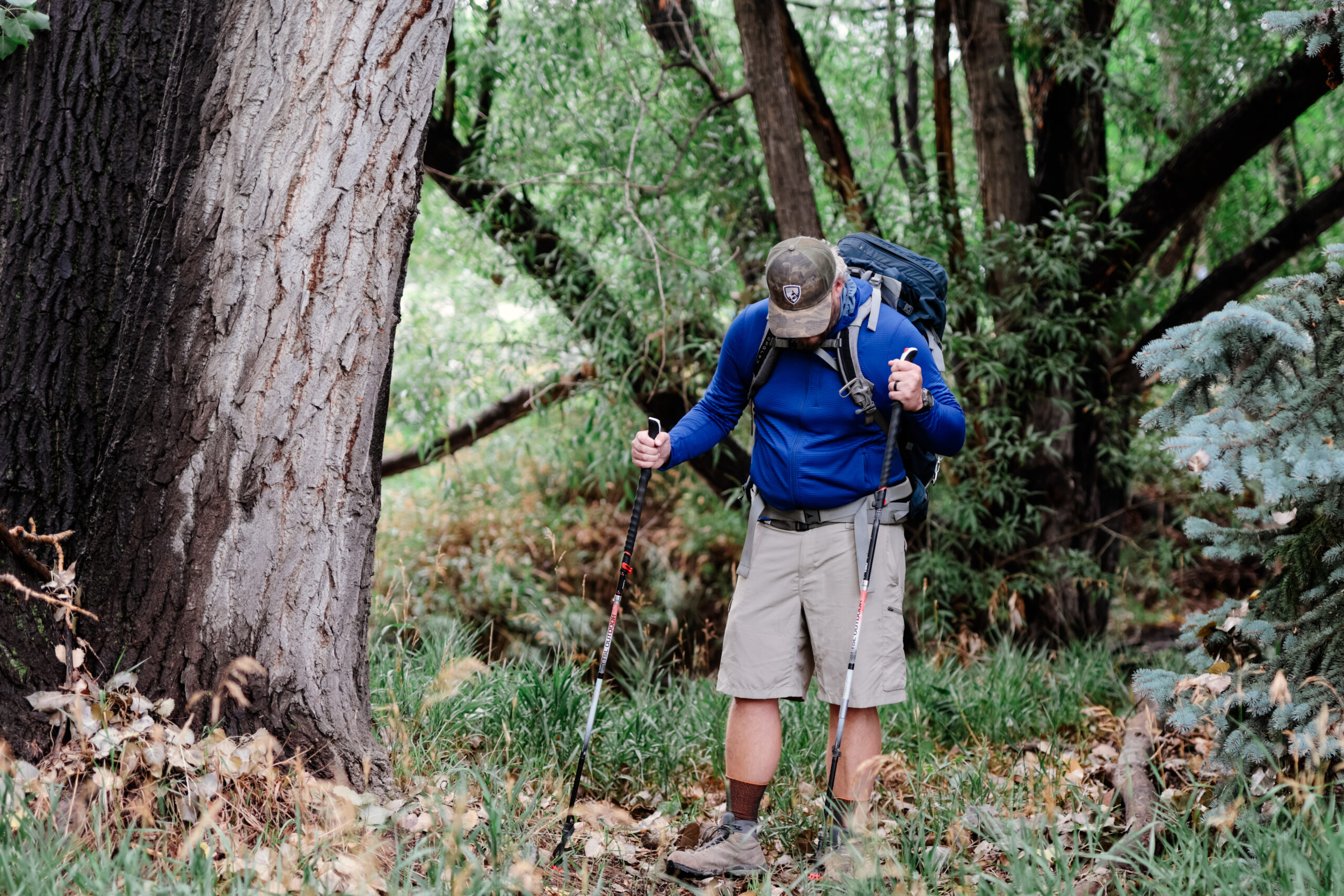 a man hikes through a forest with trekking poles wearing the Outdoor Research Vigor fleece jacket