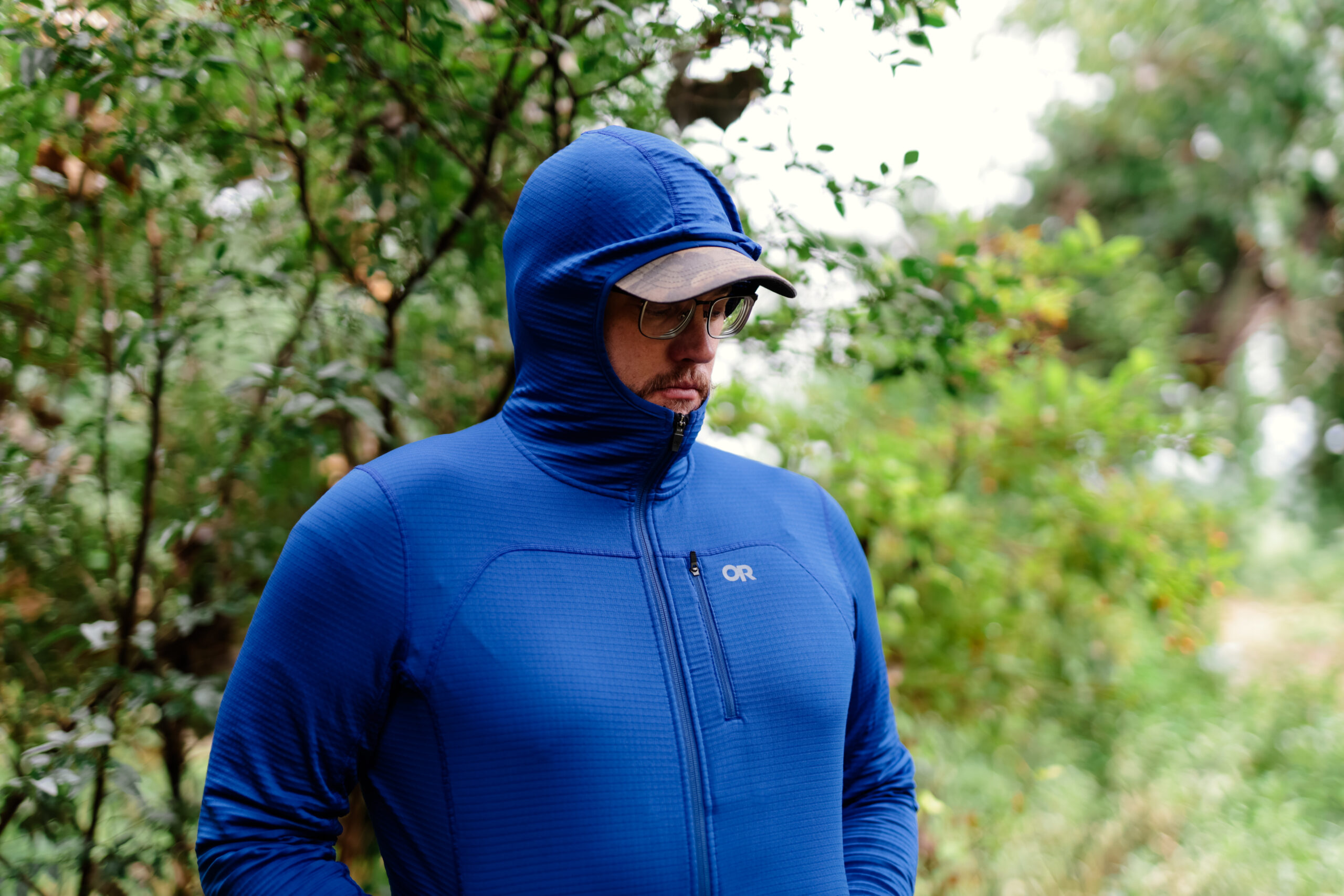 a man wearing the Outdoor Research Vigor Fleece Jacket with the hood pulled up over a ball cap