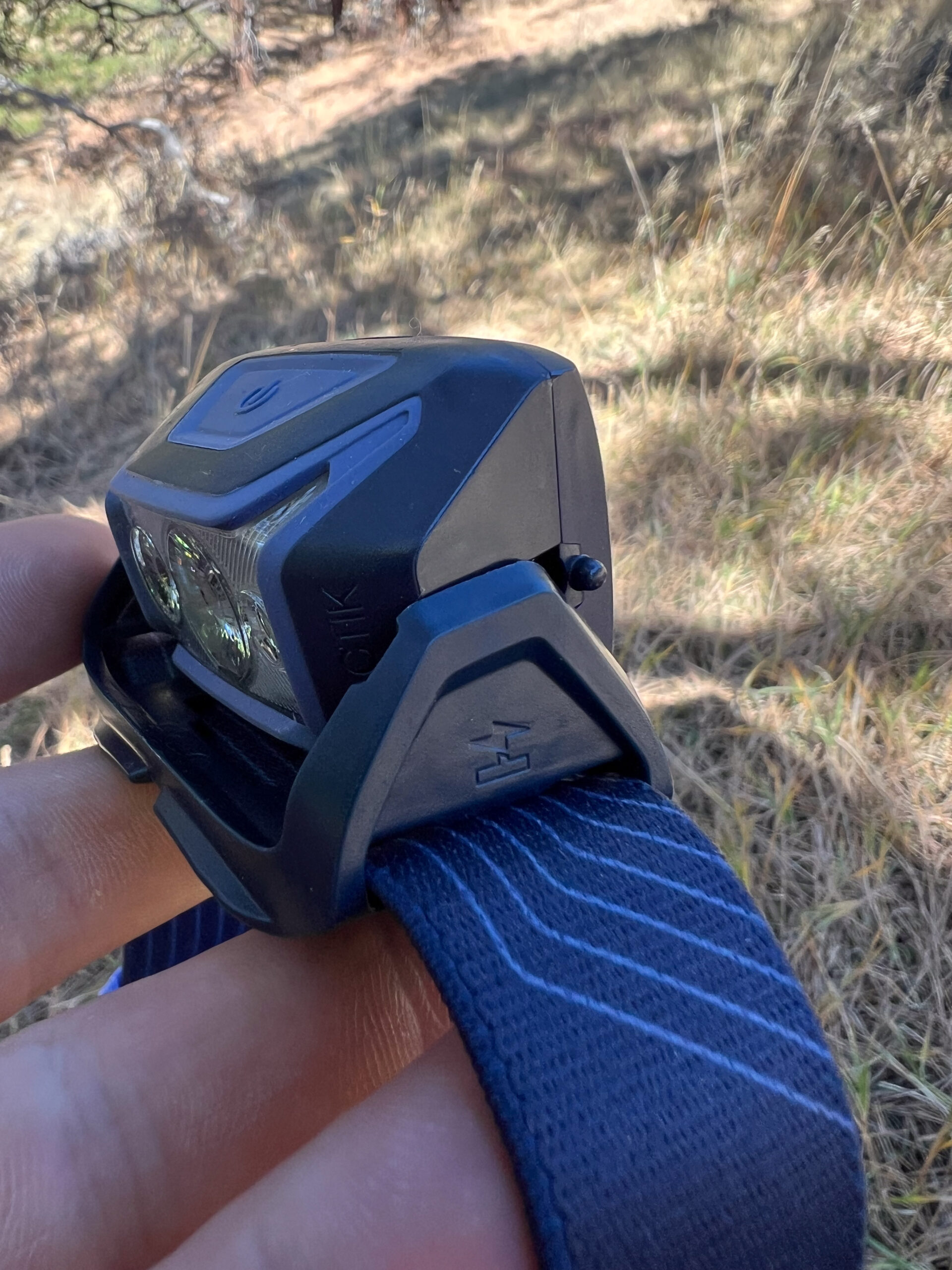 The image shows the side view of a Petzl Actik headlamp, with the focus on the body and strap. The headlamp is rotated backwards to expose the battery pack.