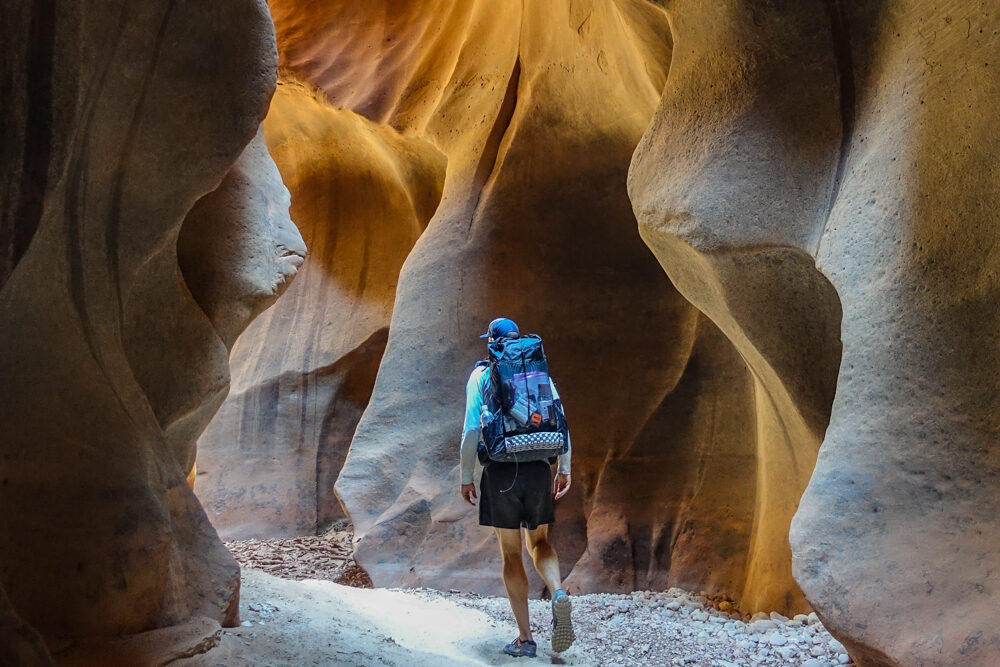 a hiker walking through a slot canyon in buckskin gulch with rounded walls of sandstone on both sides