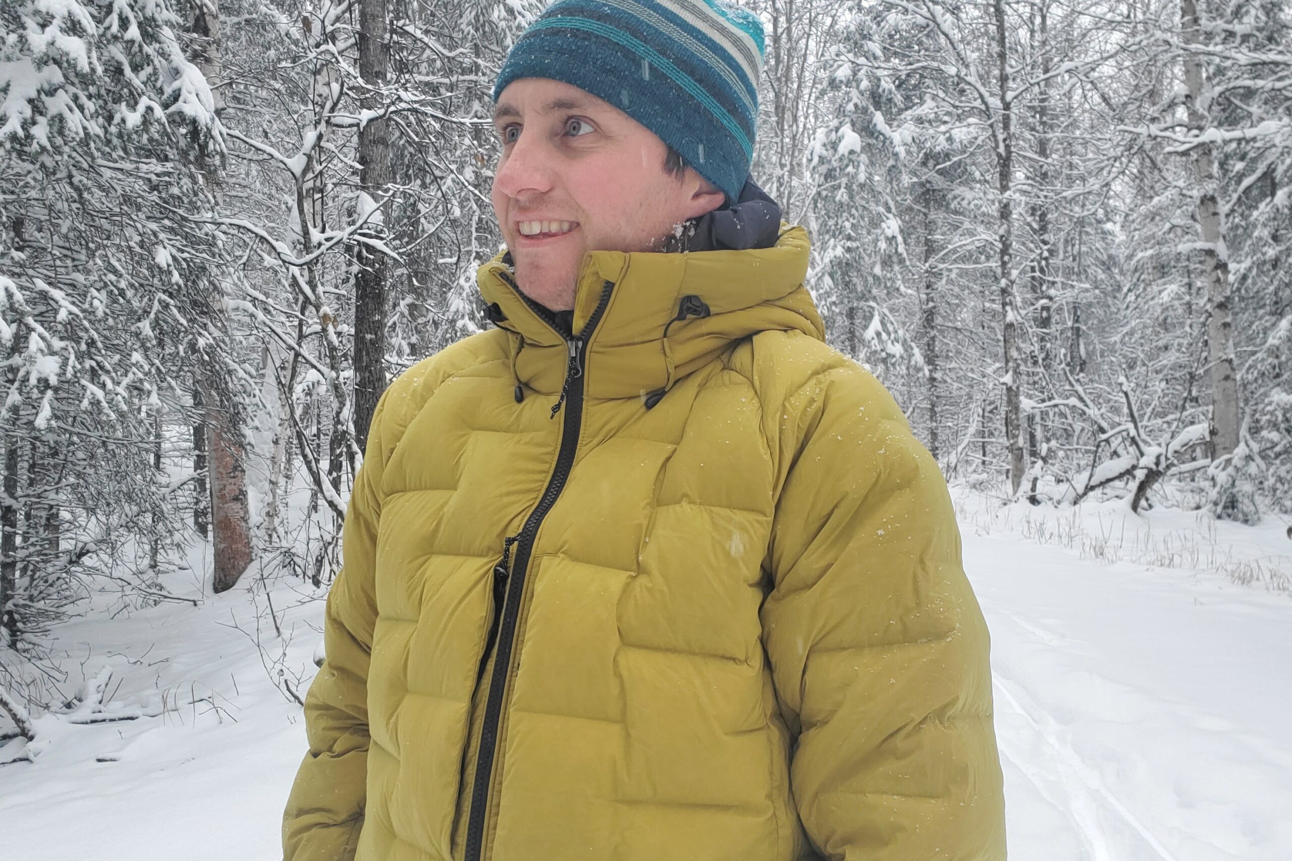 A man stands in a forest while snowing.