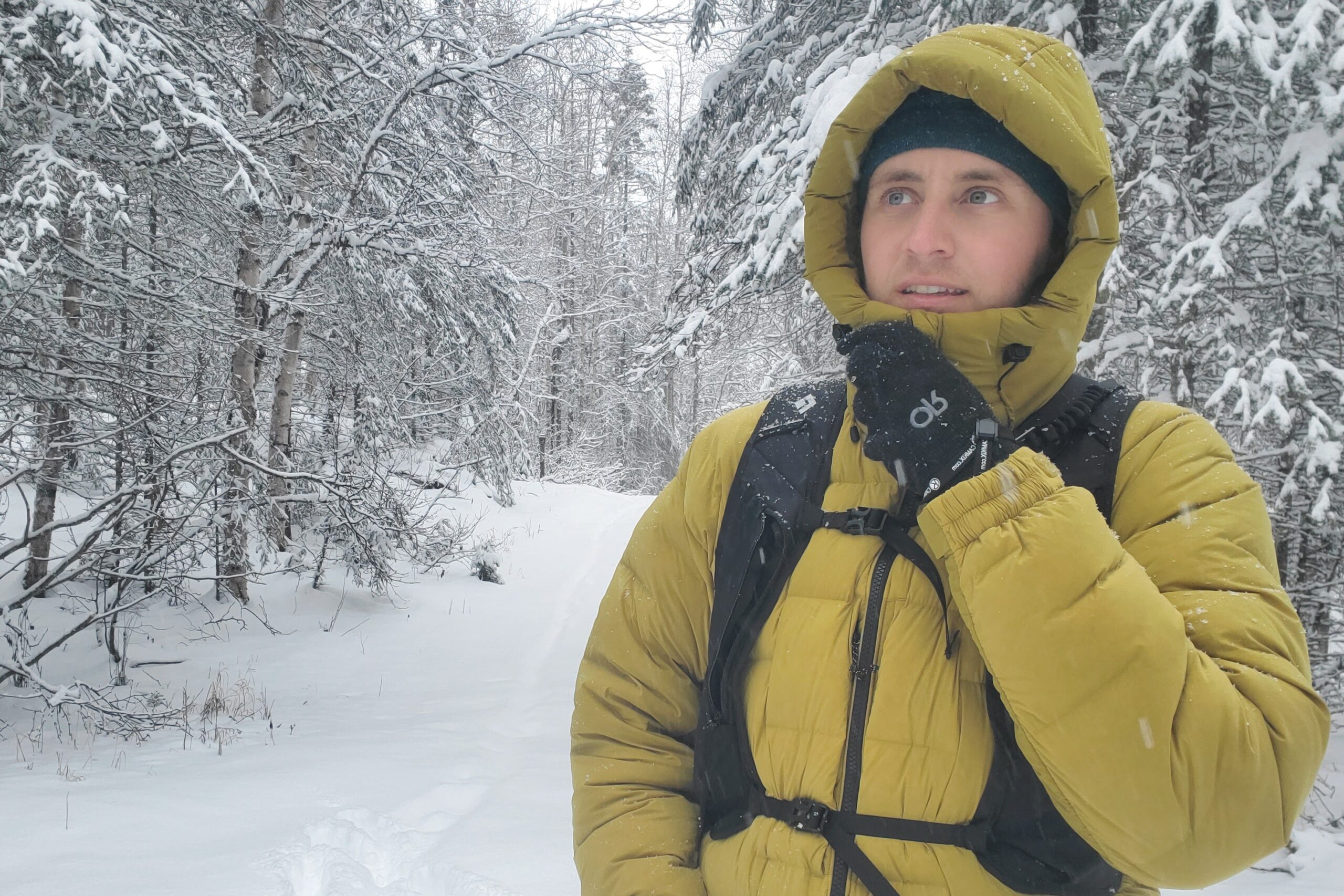 A man zips up his jacket in snowy woods.