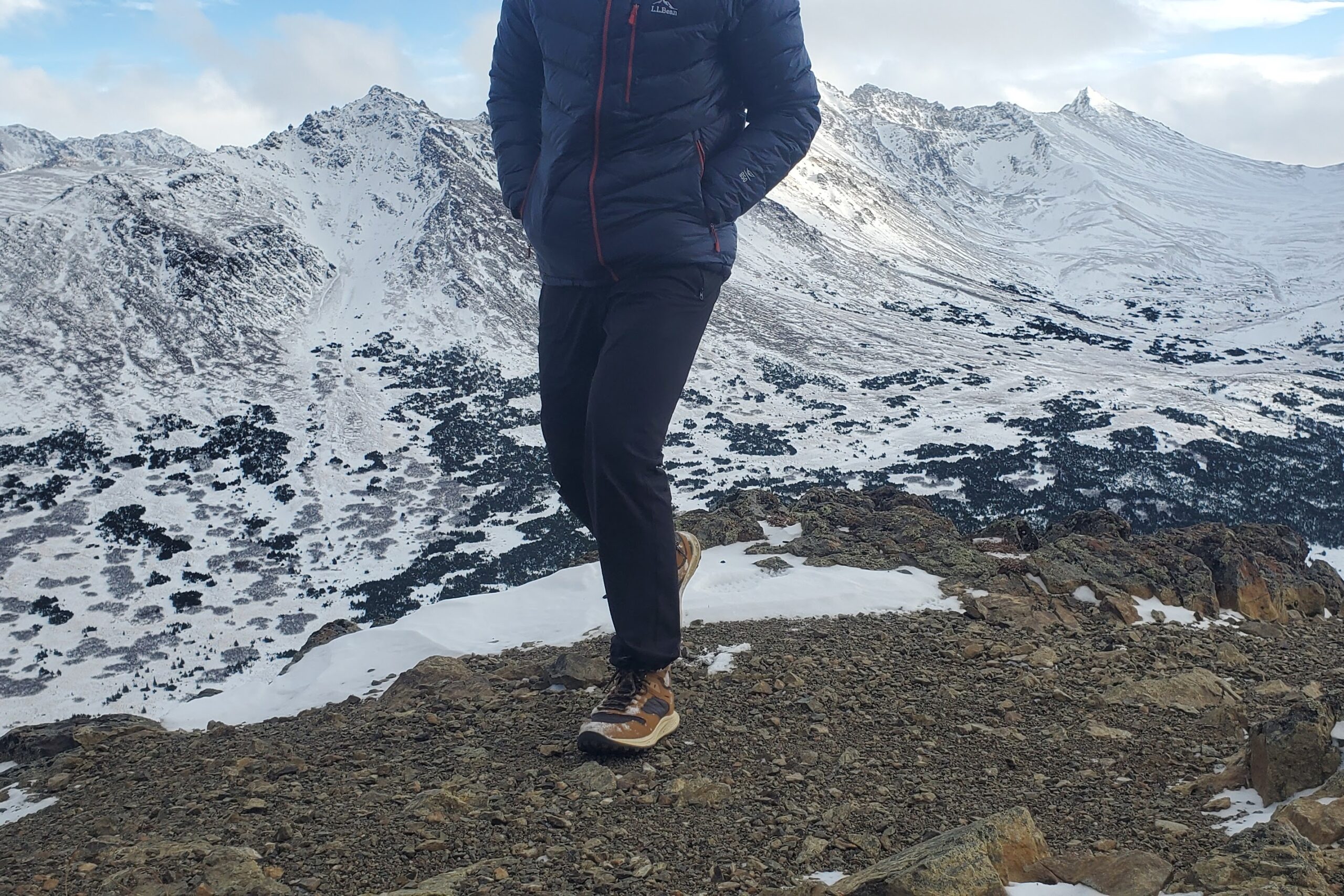 A man walks on rocks on a mountain peak.