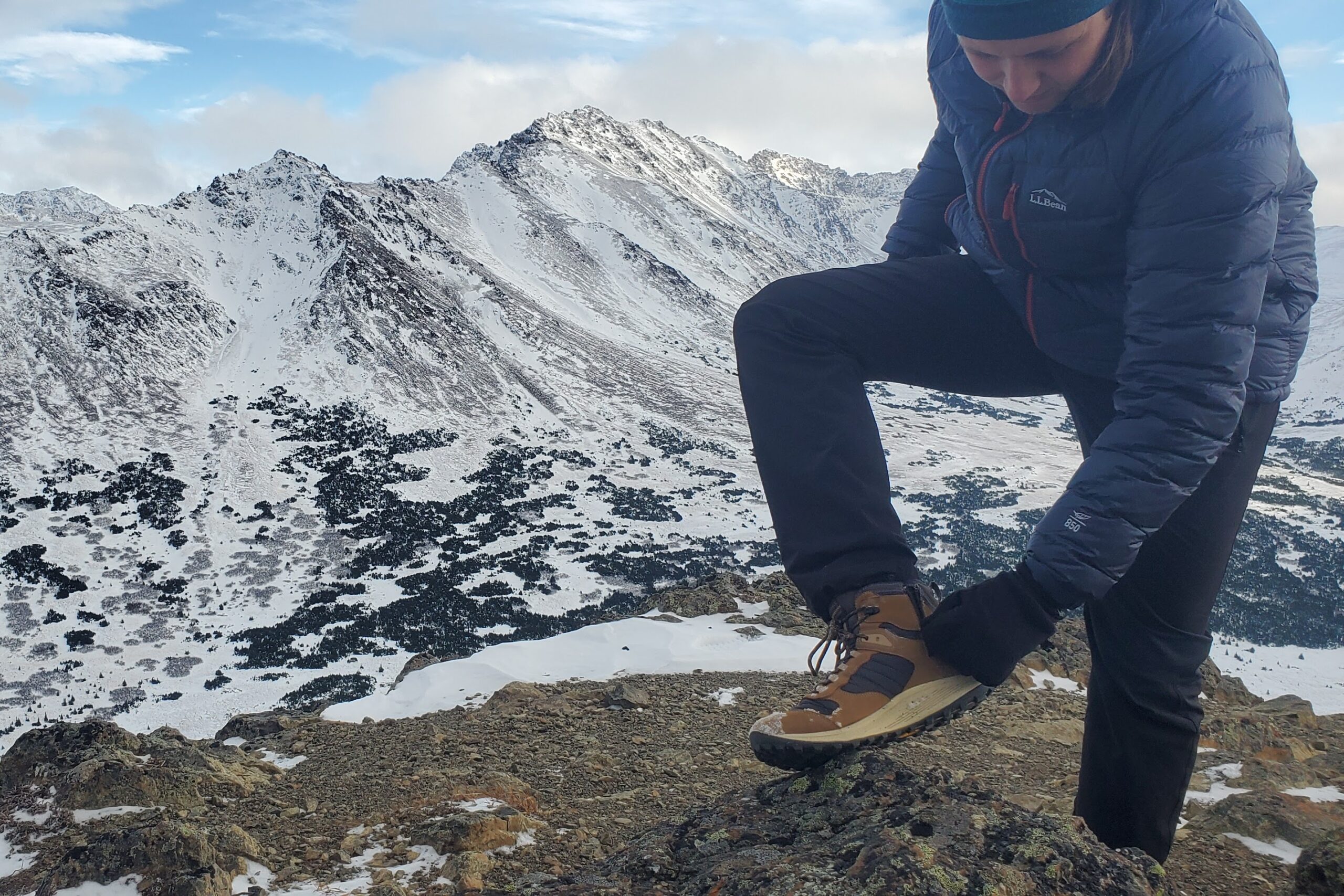 A man unzips hiking boots with a mountain backdrop.