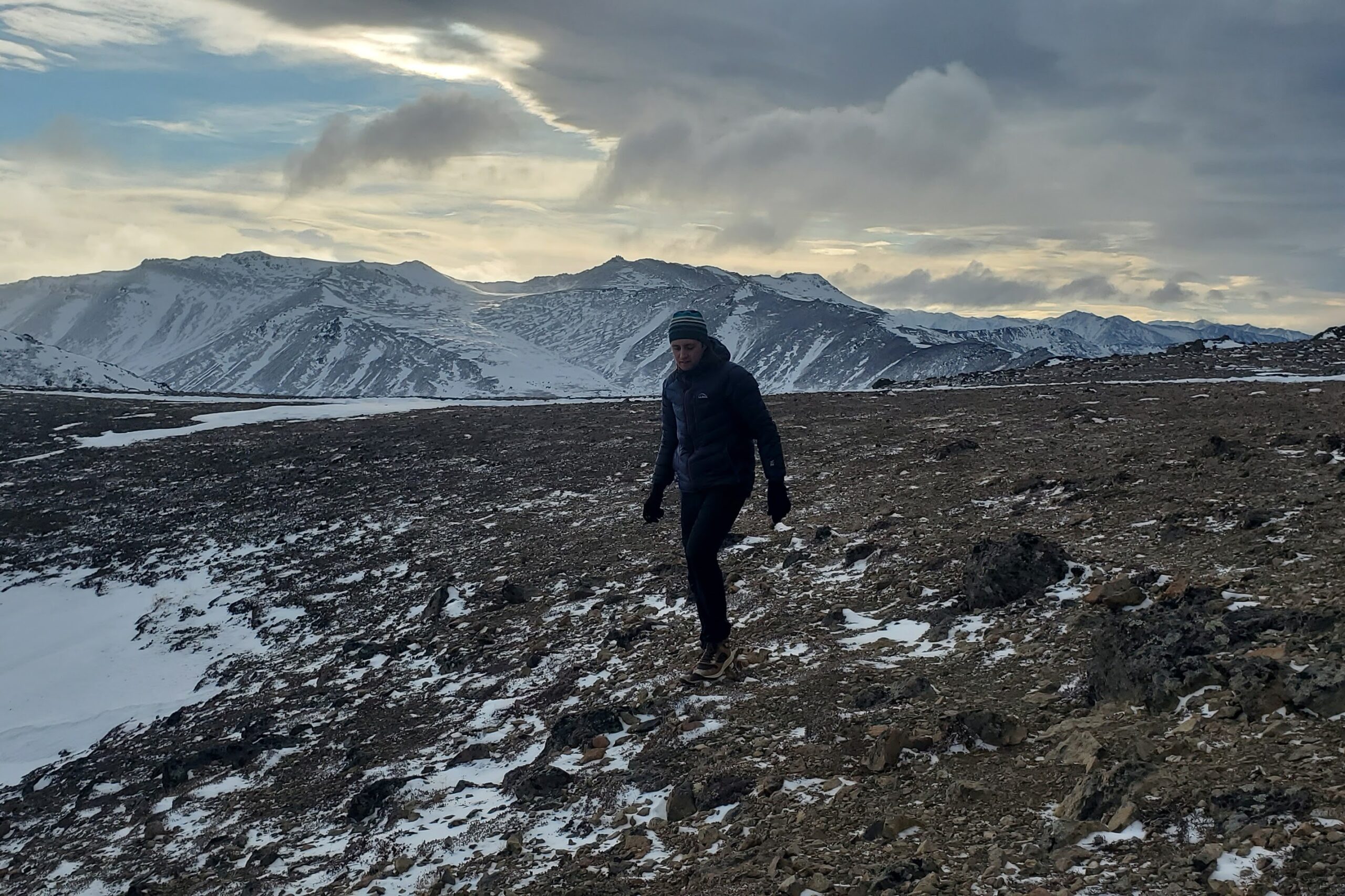 A man walks across a rocky landscape in the mountains.