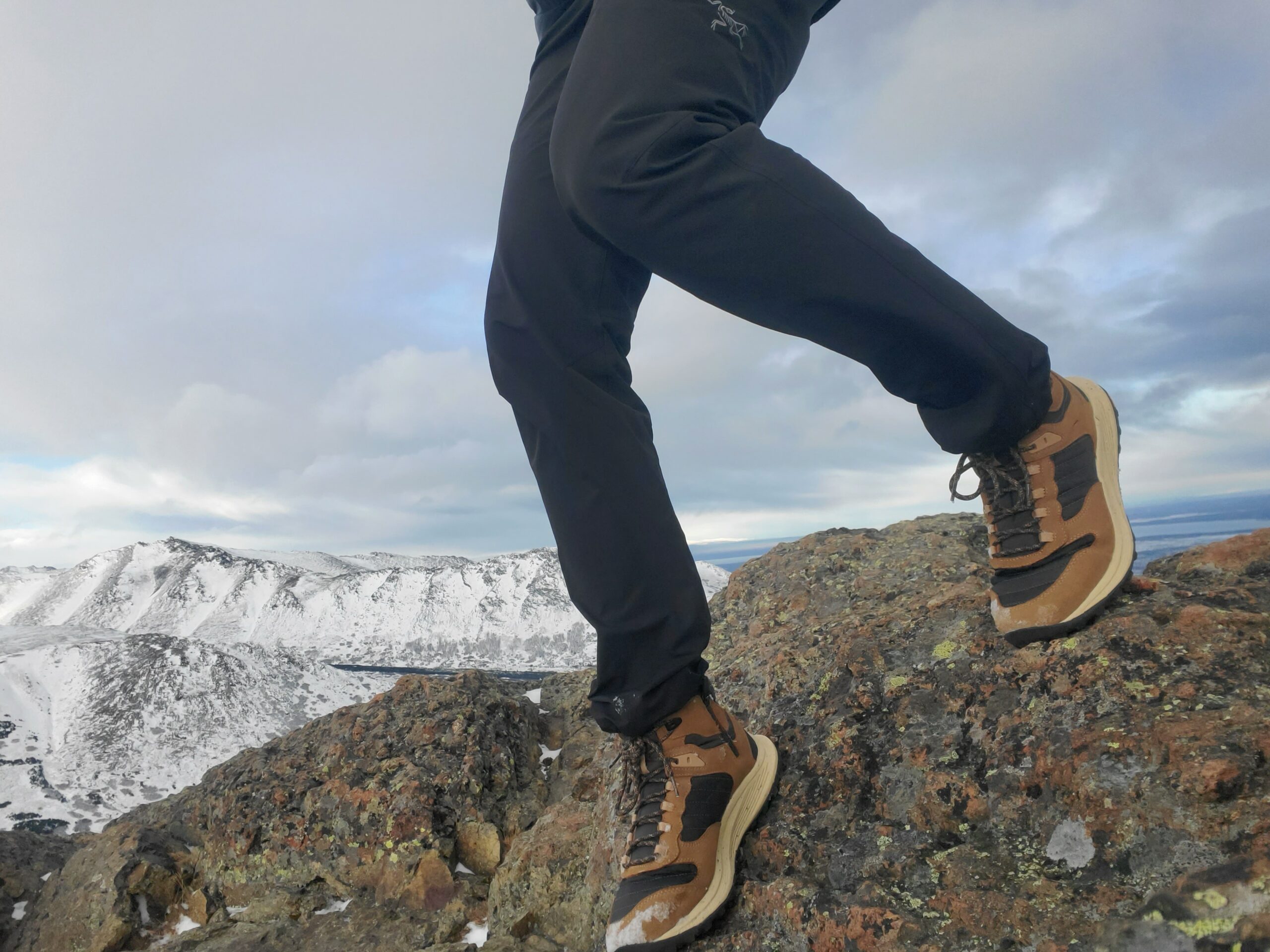 A man walks down steep rocks with winter mountains in the background.