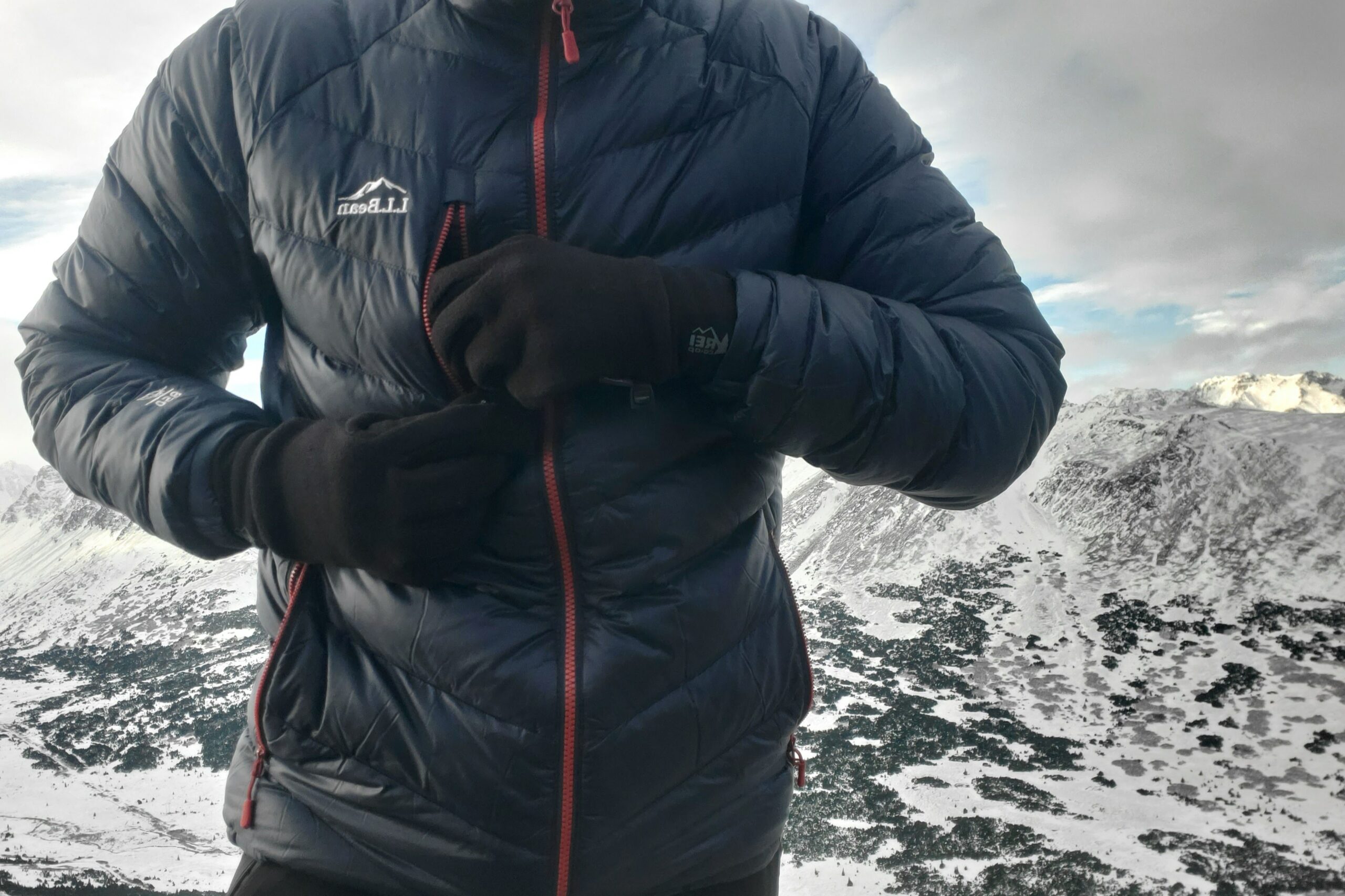 A man unzips a jacket pocket while wearing gloves.