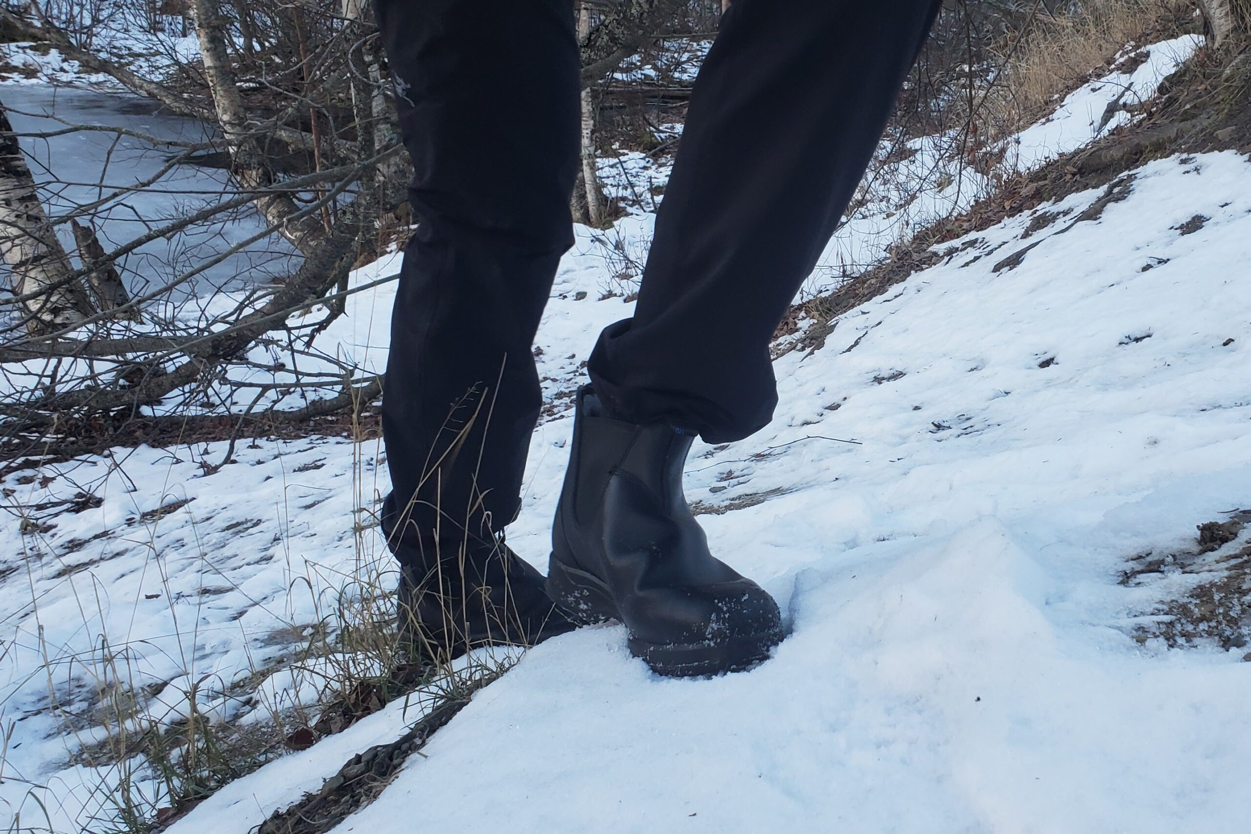 A man walks up a snowy hill in winter boots.