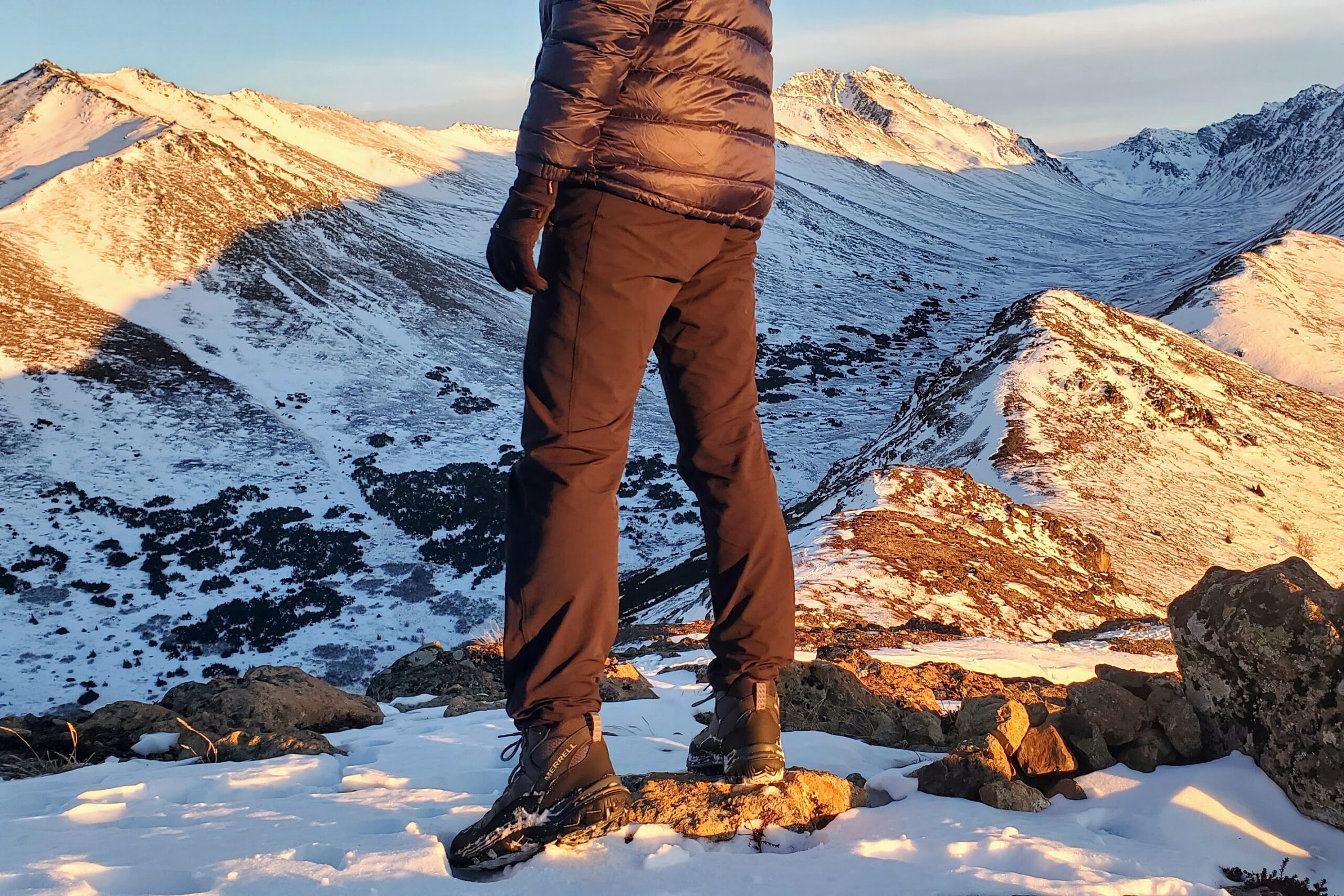 A man stands at sunset on a mountain peak.