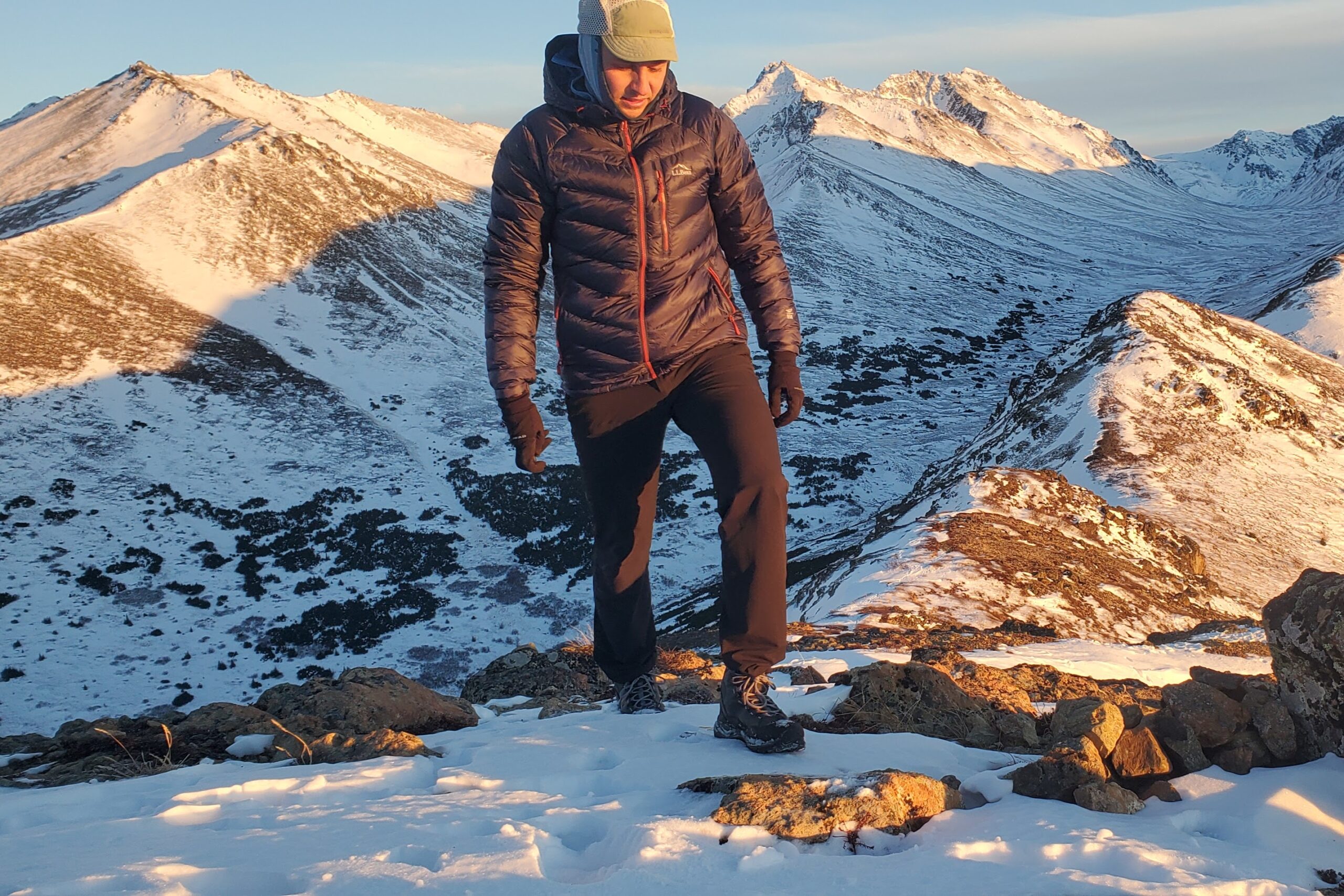 A man walks along a snowy ridgeline at sunset